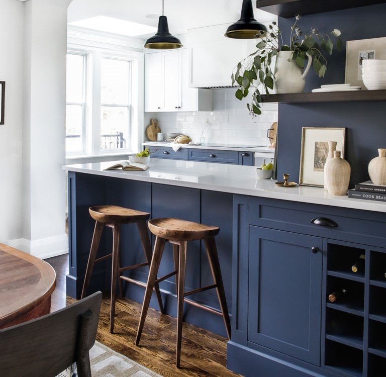 Modern kitchen with blue cabinets, white countertops, pendant lighting, and decorative items on the counter and shelves.
