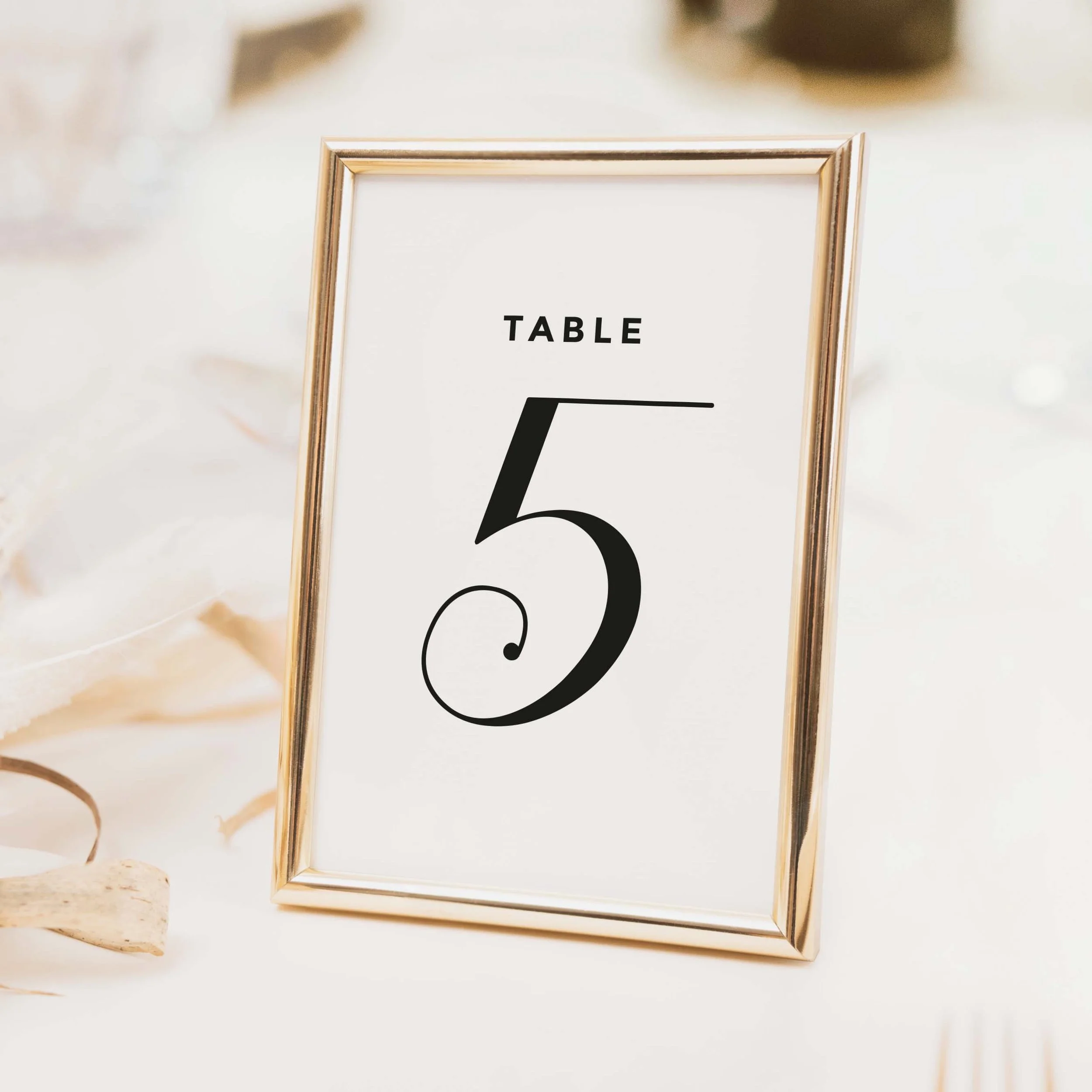 Calligraphy wedding table number with bold flowing script numeral on a clean white background printed on luxury off-white textured card