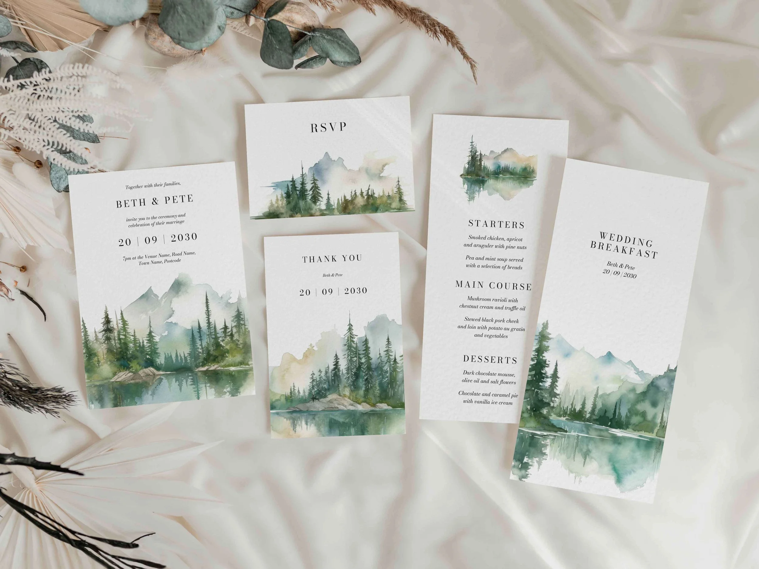 Full Wilderness wedding stationery suite flat lay showing invitations, RSVP cards and coordinating pieces with watercolour mountain lake landscape