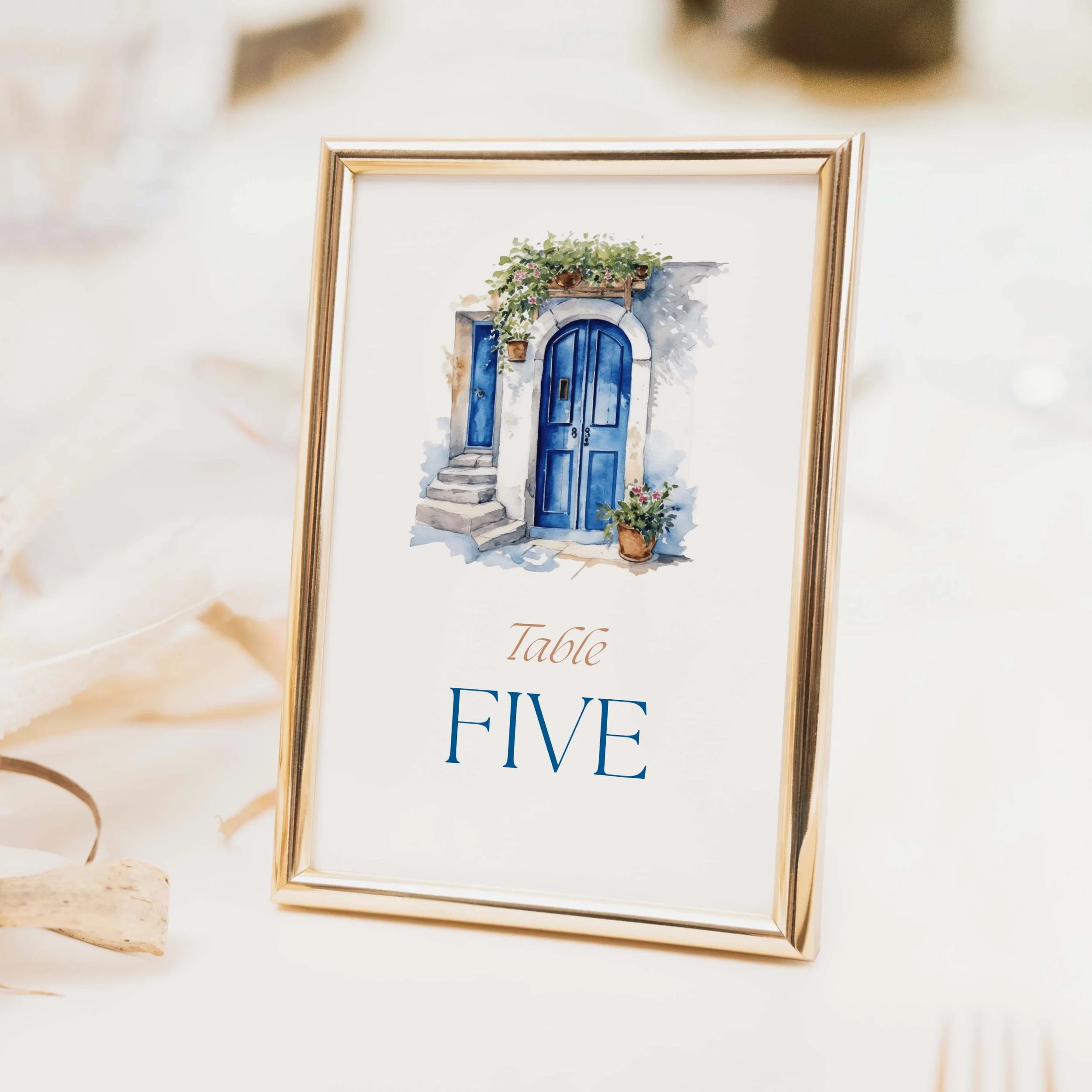 Santorini wedding table number with illustrated Greek island blue door and Mediterranean arch and elegant script typography on luxury off-white card