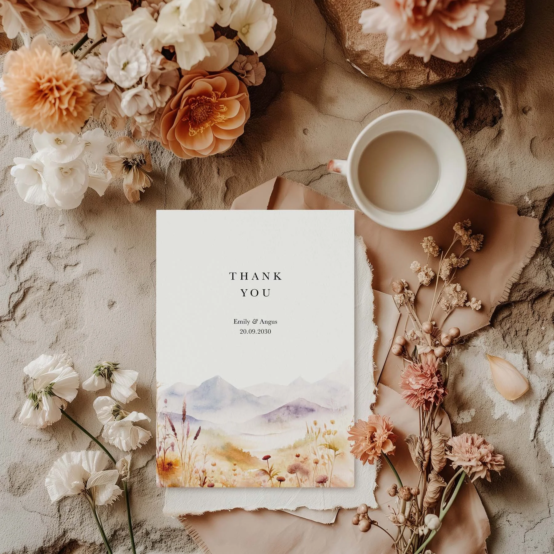 Scenic wedding thank you card with a watercolour landscape featuring purple mountains and a golden wildflower meadow, styled with dried flowers and a white cup on a neutral background