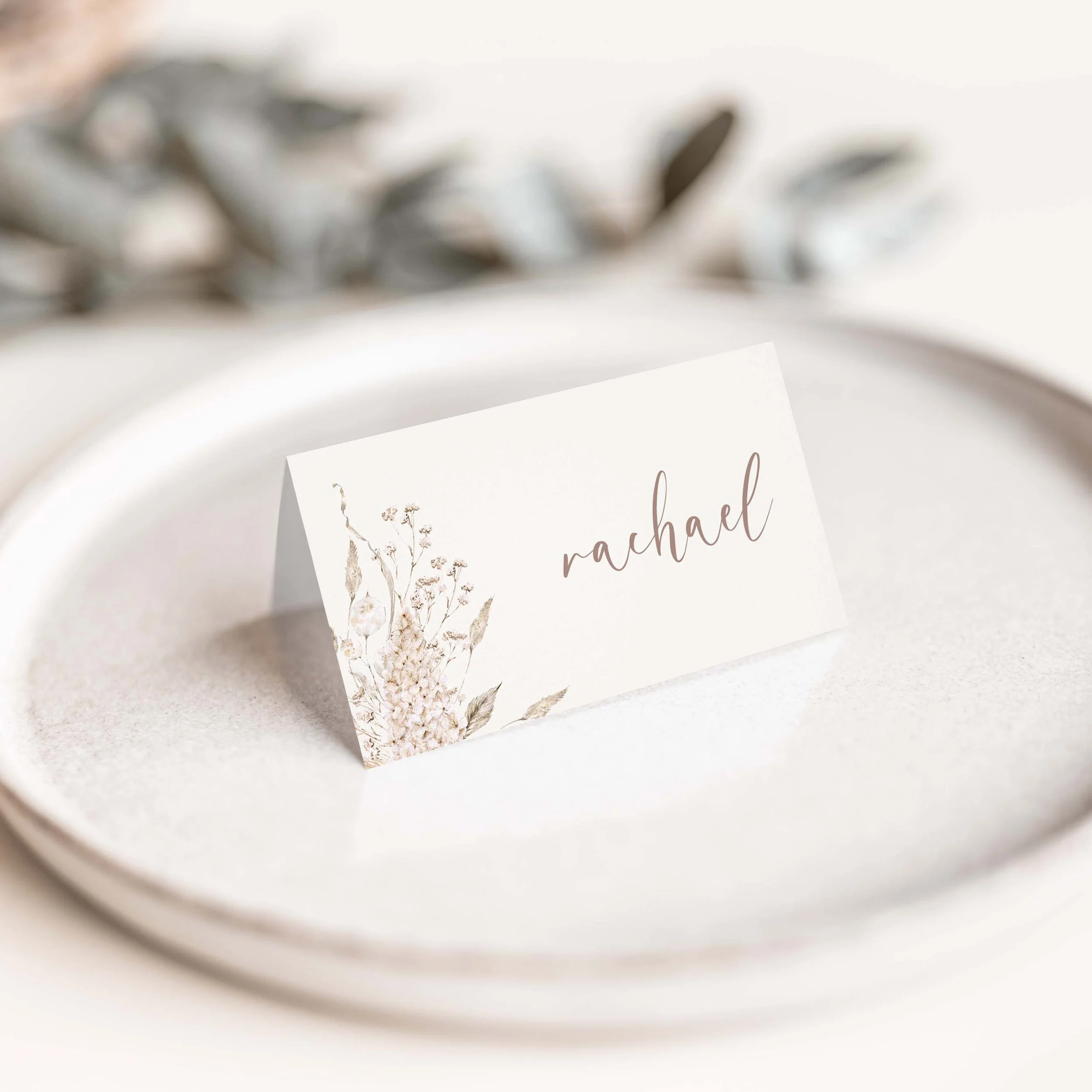 Boho neutral wedding place card with soft beige tones and flowing script typography on luxury off-white card