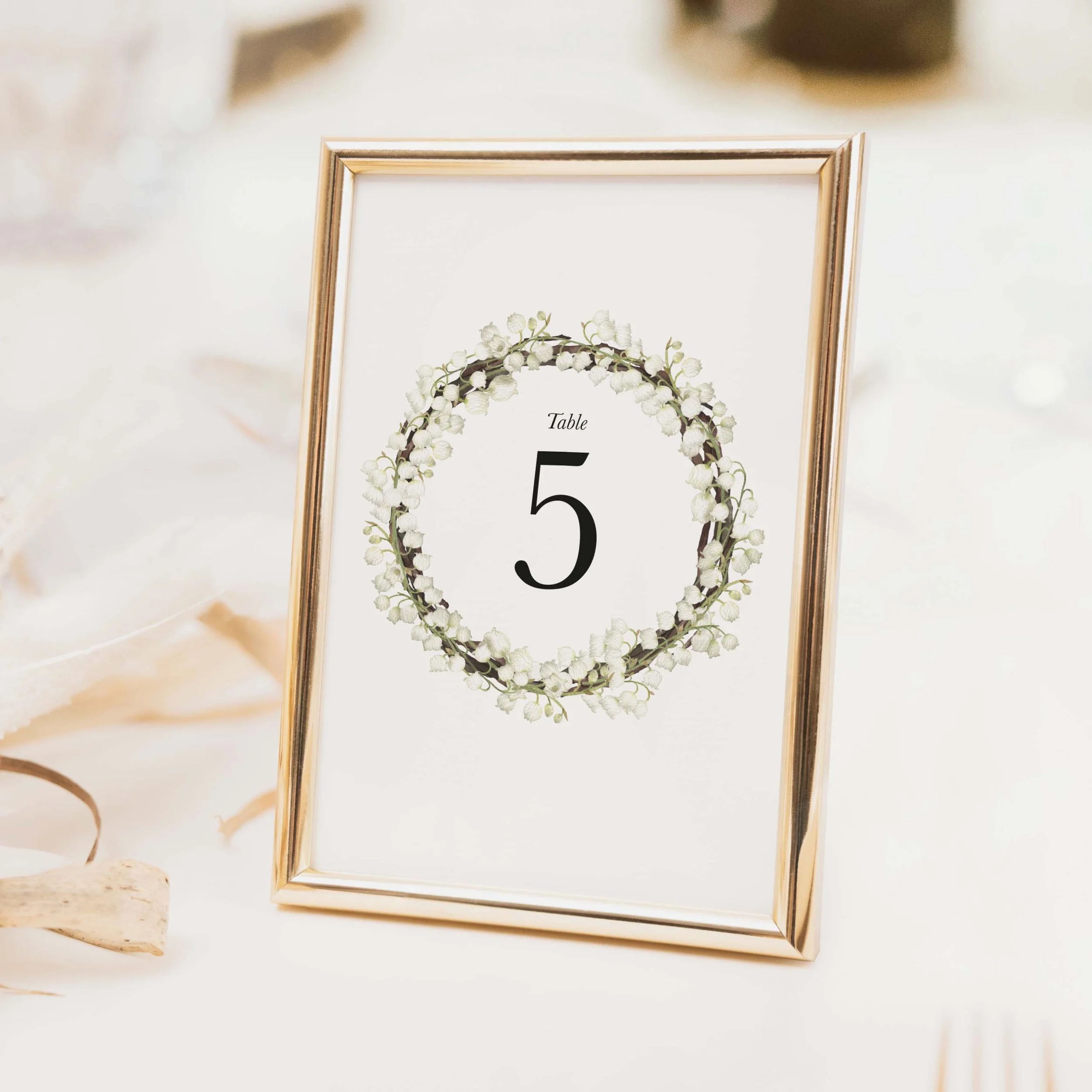 Garden wedding table number with circular botanical wreath border framing a clean central numeral on luxury off-white card