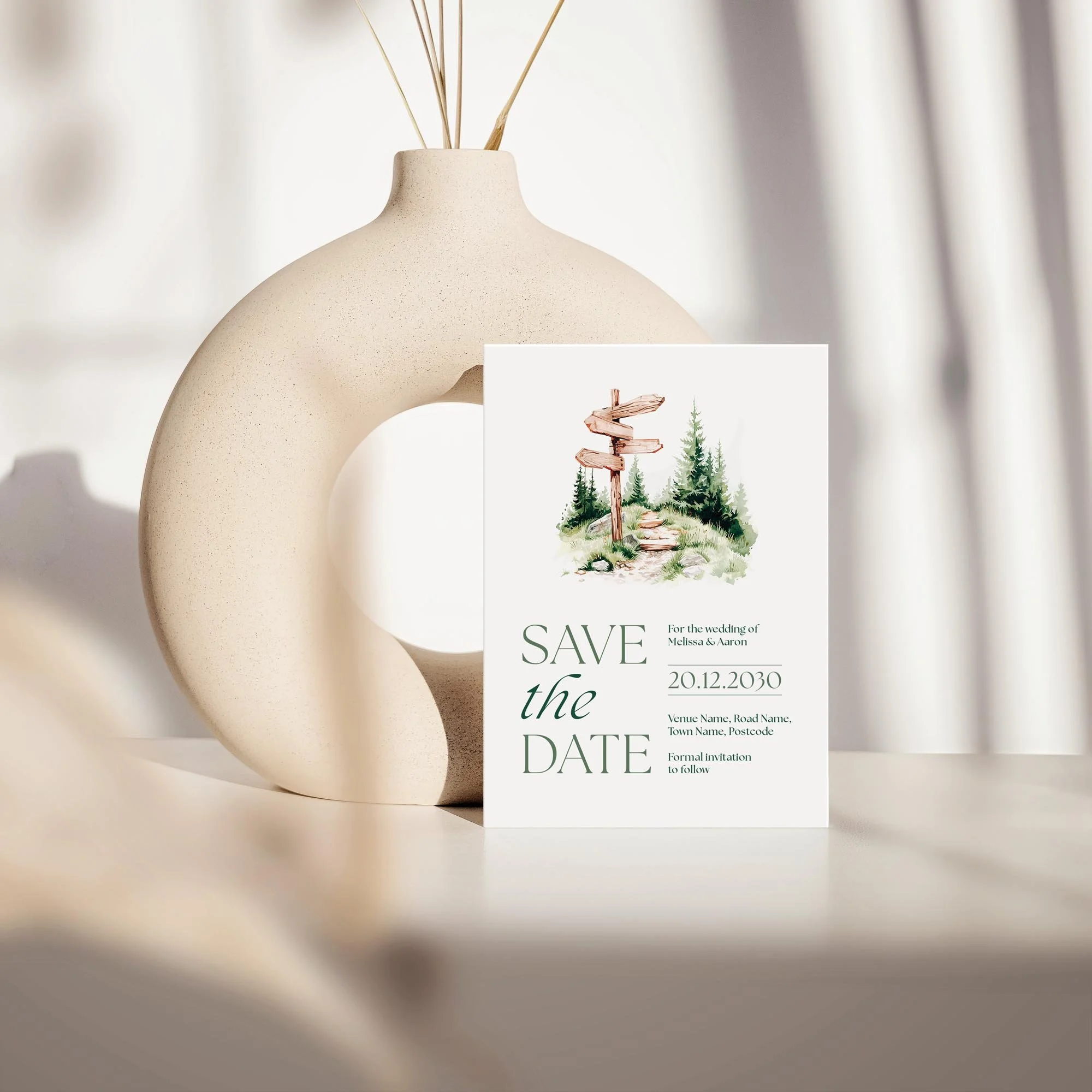 Adventure save the date card with mountain and forest illustration displayed against a cream ceramic vase on a neutral background