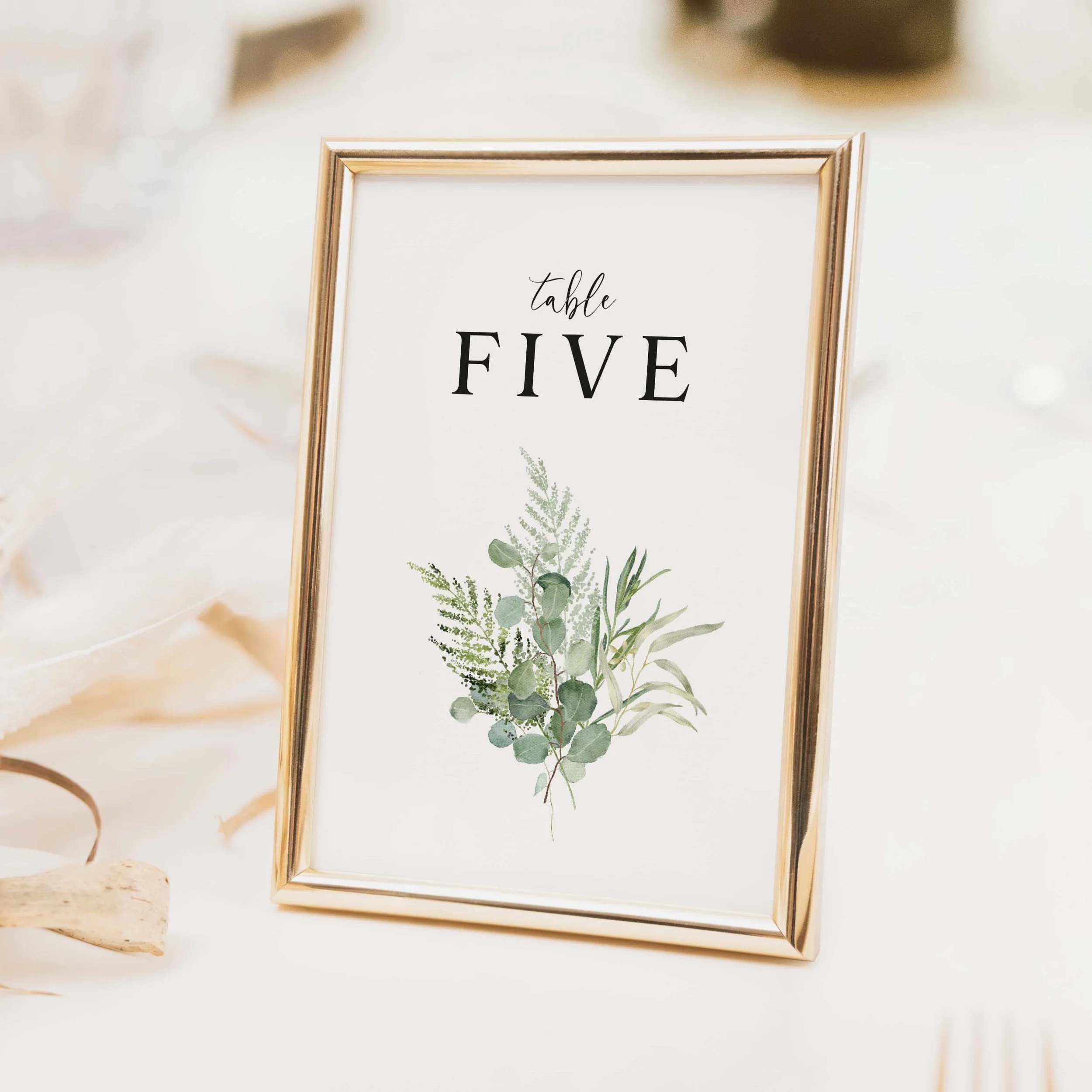 Greenery wedding table number with sage and olive botanical foliage illustration and elegant script typography on luxury off-white card