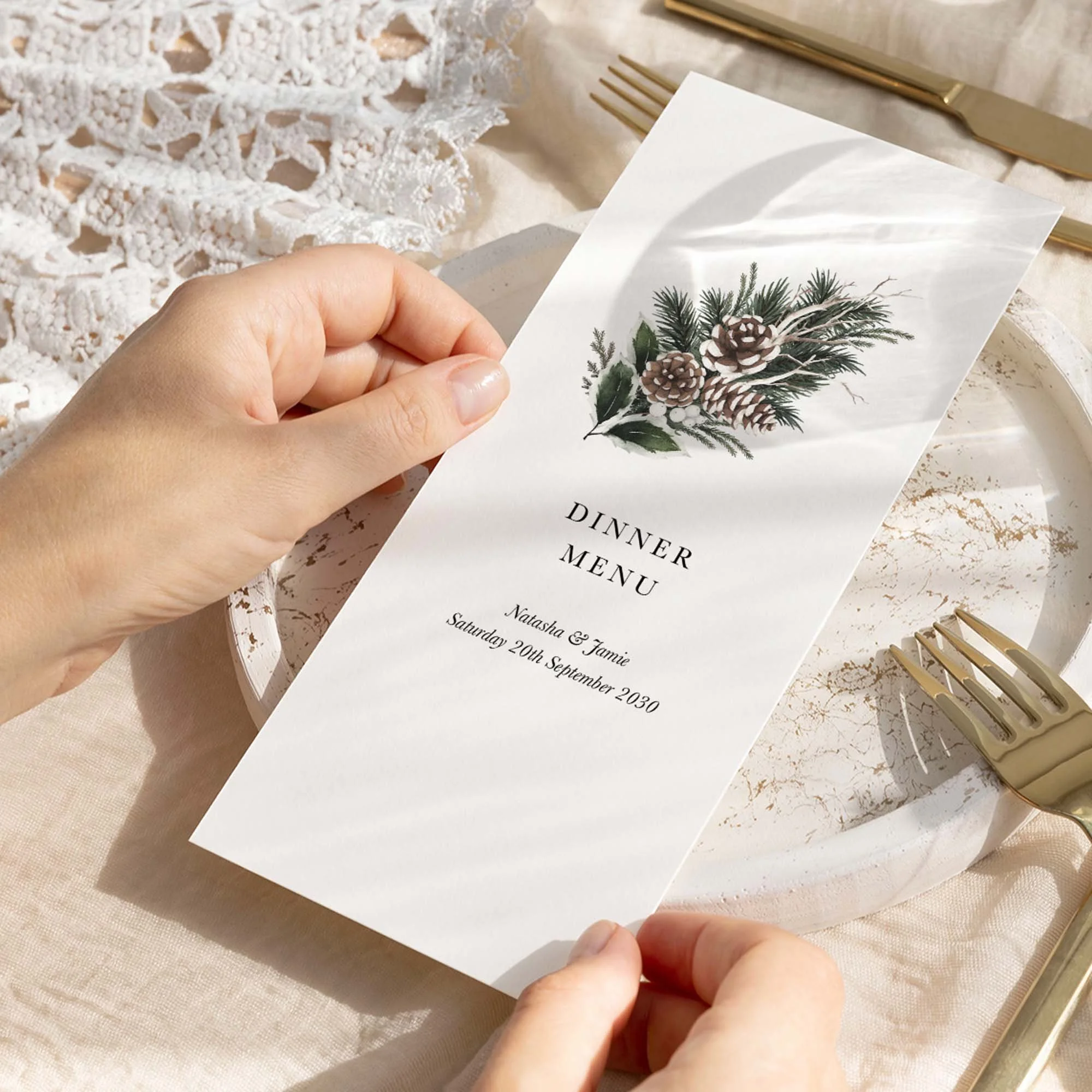 Hand holding a Woodland wedding breakfast menu card with a pine cone, cotton stem and evergreen botanical illustration