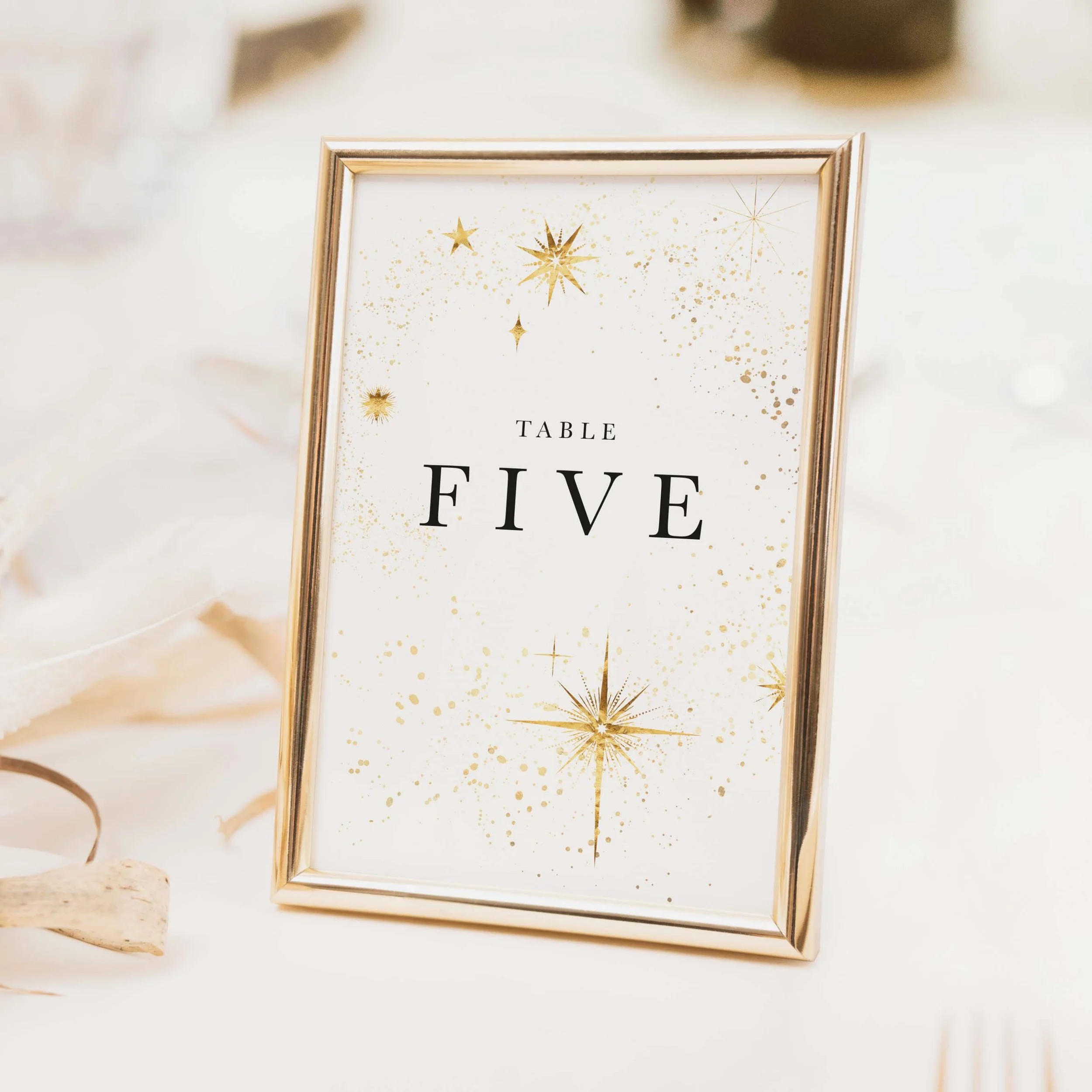 Celestial wedding table number with gold star and moon illustration and refined serif typography on a white background printed on luxury off-white textured card