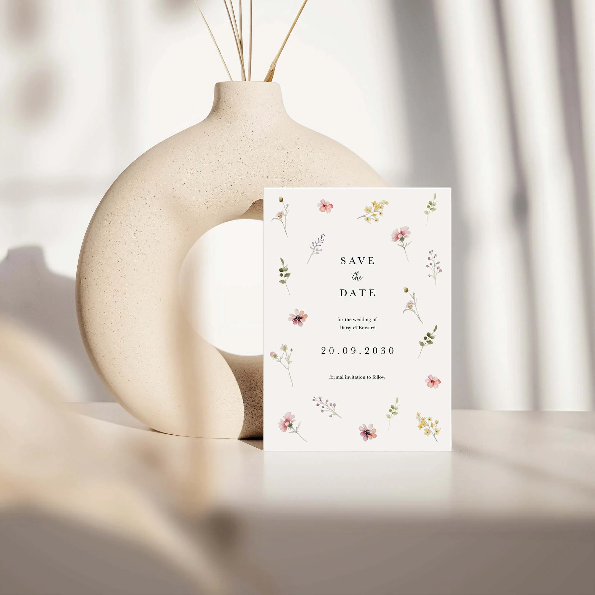 Flora save the date card with scattered wildflower design displayed against a cream ceramic vase on a neutral background