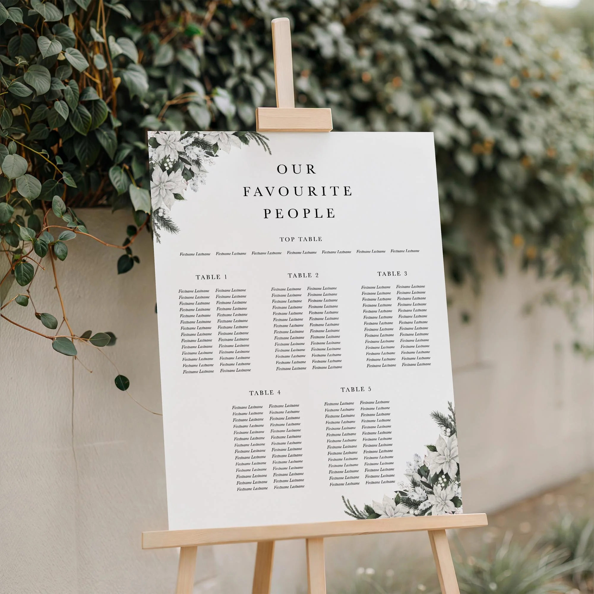 Winter Frost wedding seating plan displayed on a wooden easel, featuring a white poinsettia botanical wreath design with multiple guest tables