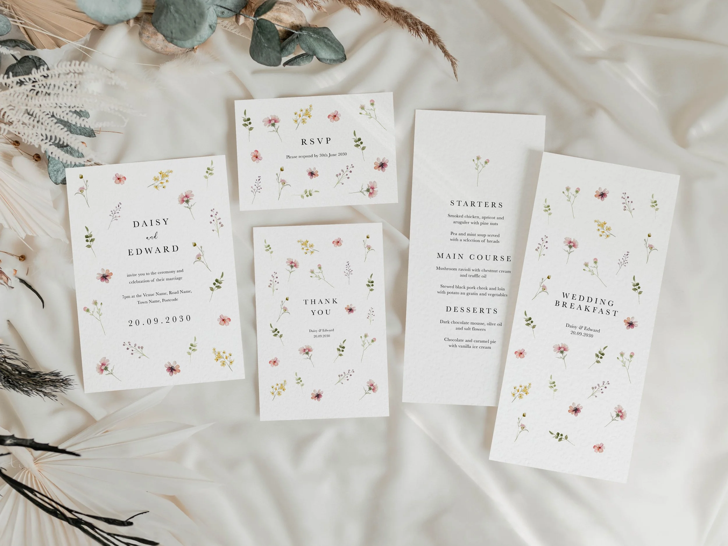 Full Flora wedding stationery suite flat lay showing invitations, RSVP cards and coordinating pieces with scattered pastel wildflower design