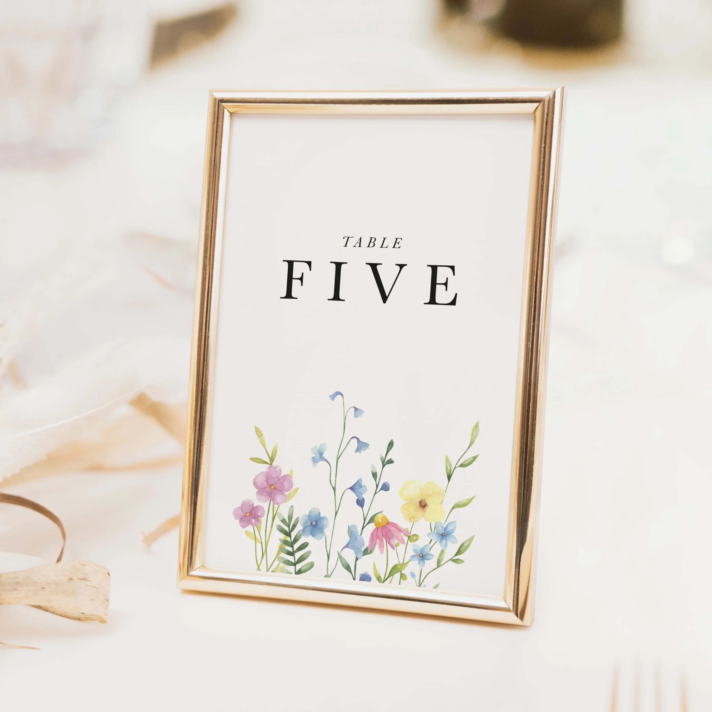 Wildflower wedding table number with vibrant colourful scattered meadow floral illustration and bold typography on luxury off-white textured card