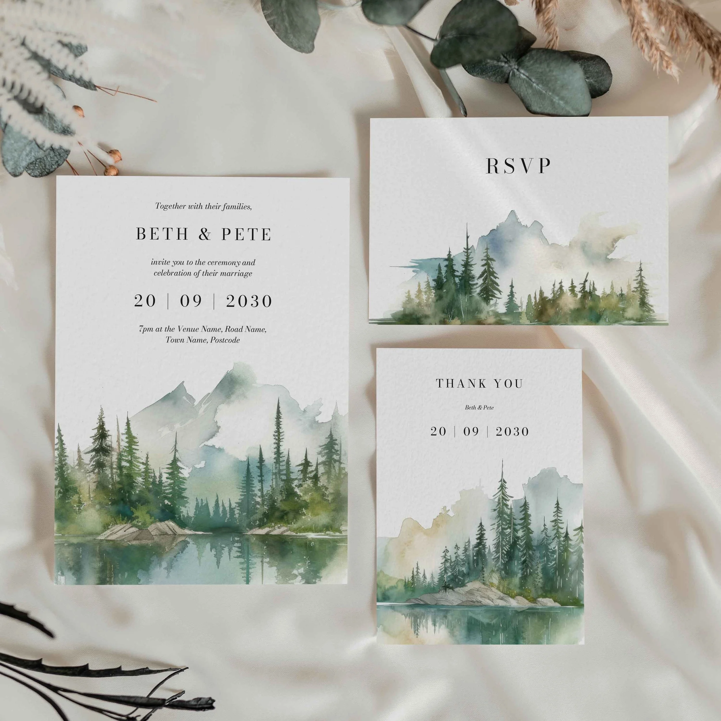 The Wilderness wedding stationery collection showing invitation and menu cards with a serene watercolour mountain lake and pine forest landscape in soft sage green tones