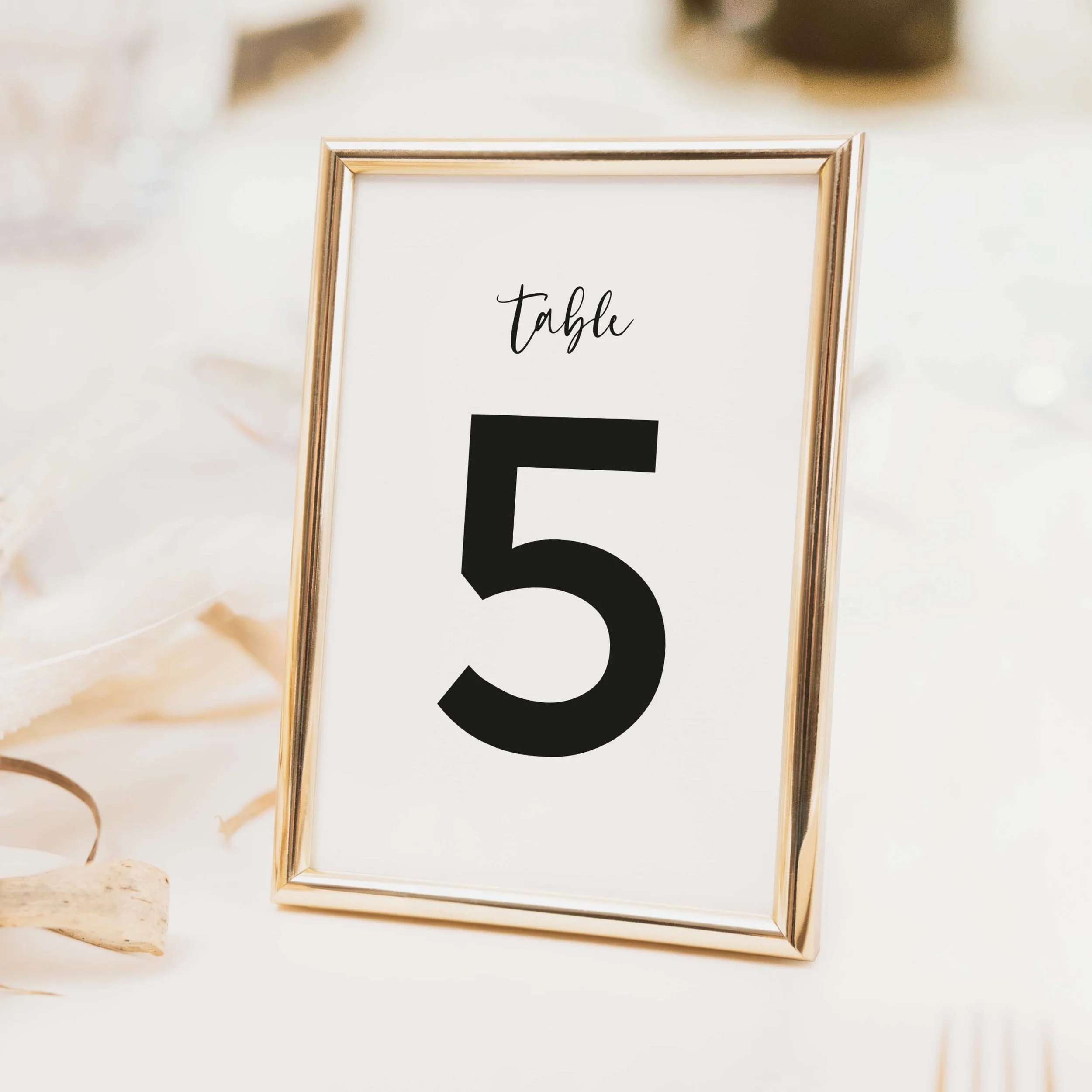 Script wedding table number with large bold numeral and delicate calligraphy script label in contrasting typography on luxury off-white card