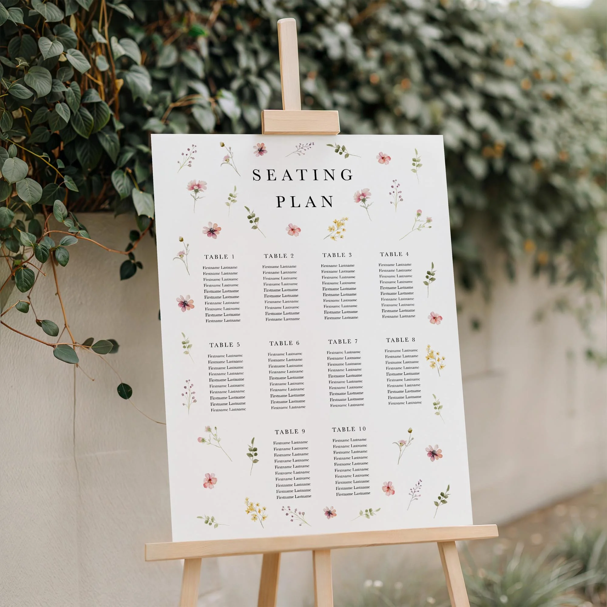 Flora wedding seating plan displayed on a wooden easel, featuring a scattered pastel wildflower border with multiple guest tables