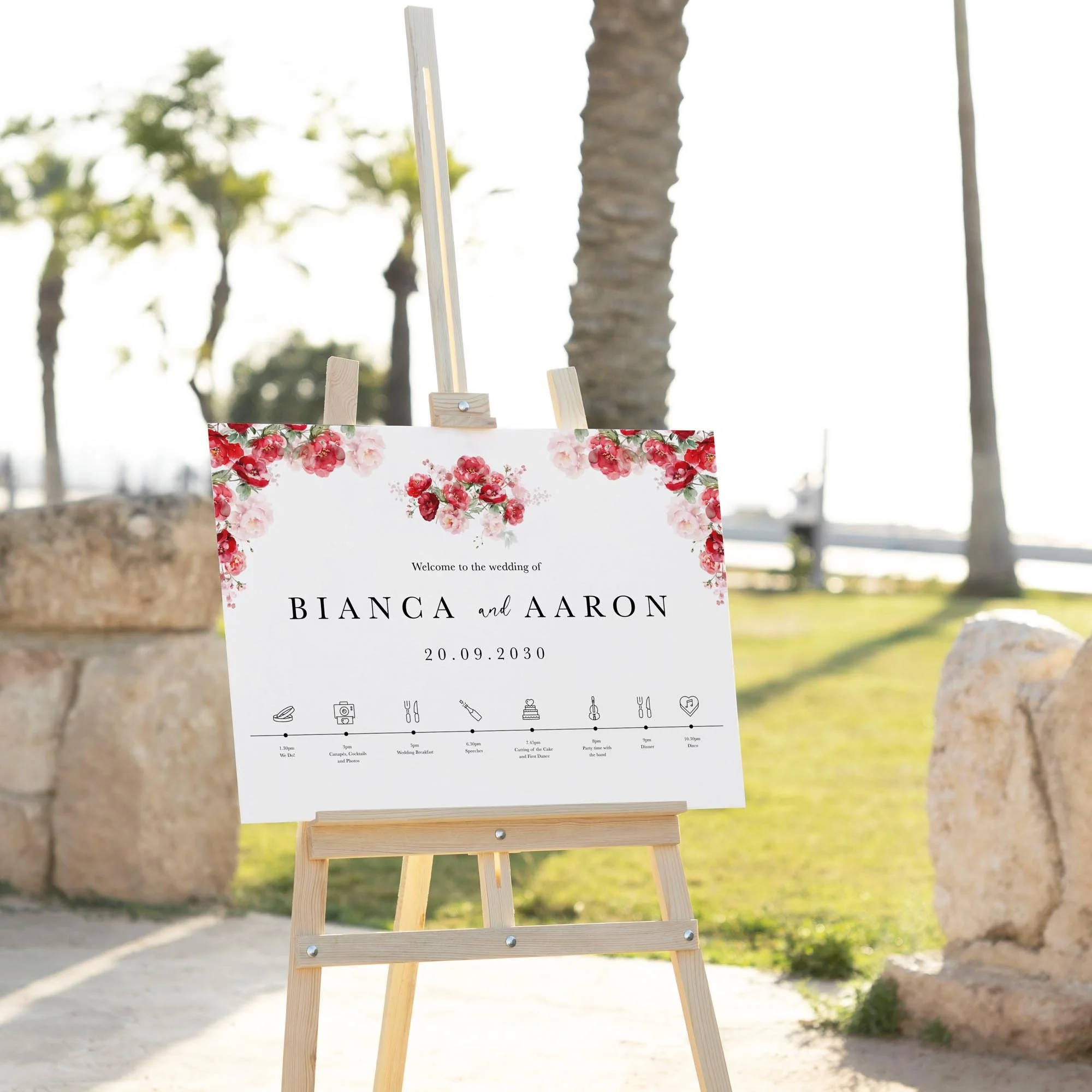 Red Floral wedding welcome sign displayed outdoors at a wedding venue on an easel