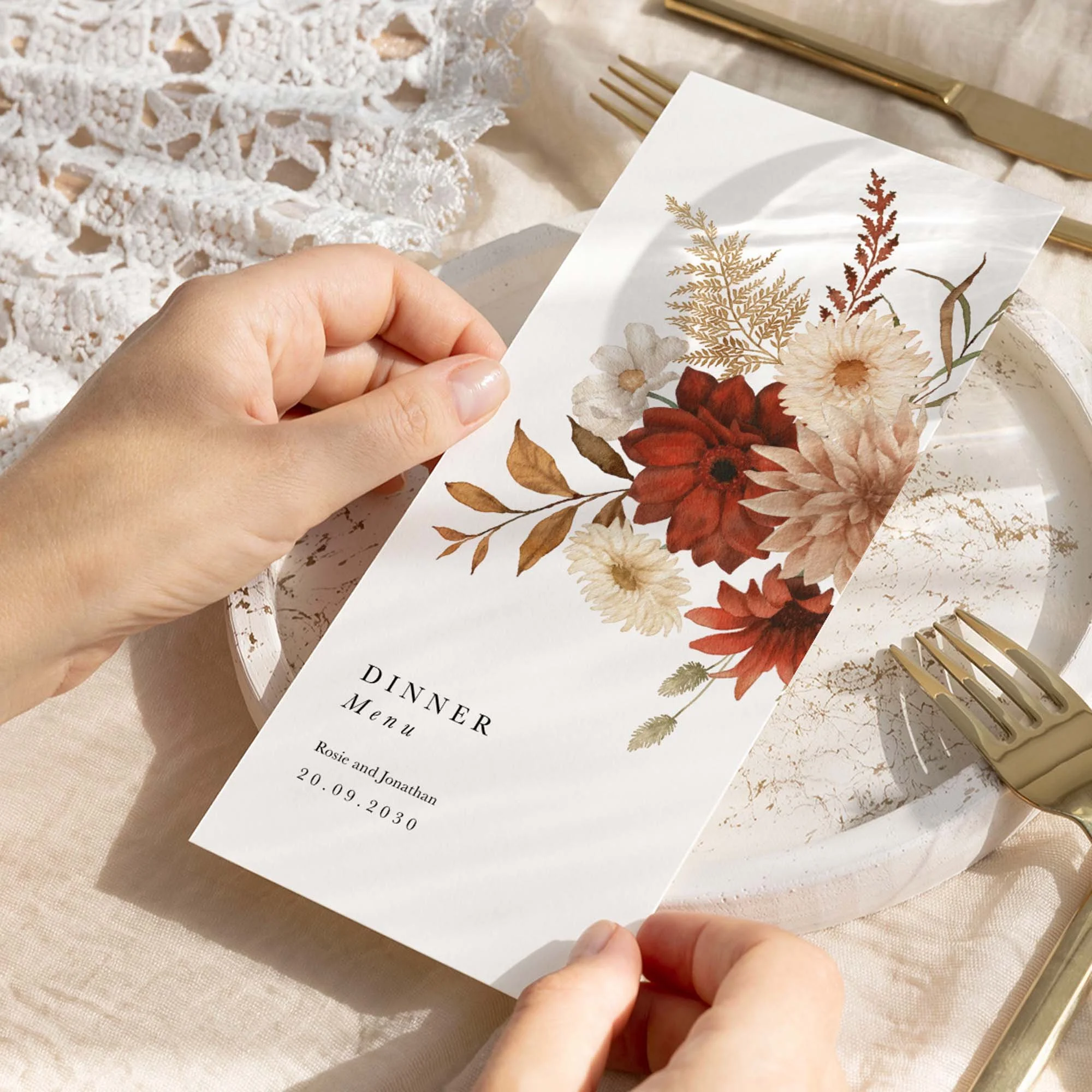 Hand holding a Rustic wedding breakfast menu card with a crimson dahlia and cream chrysanthemum floral corner illustration