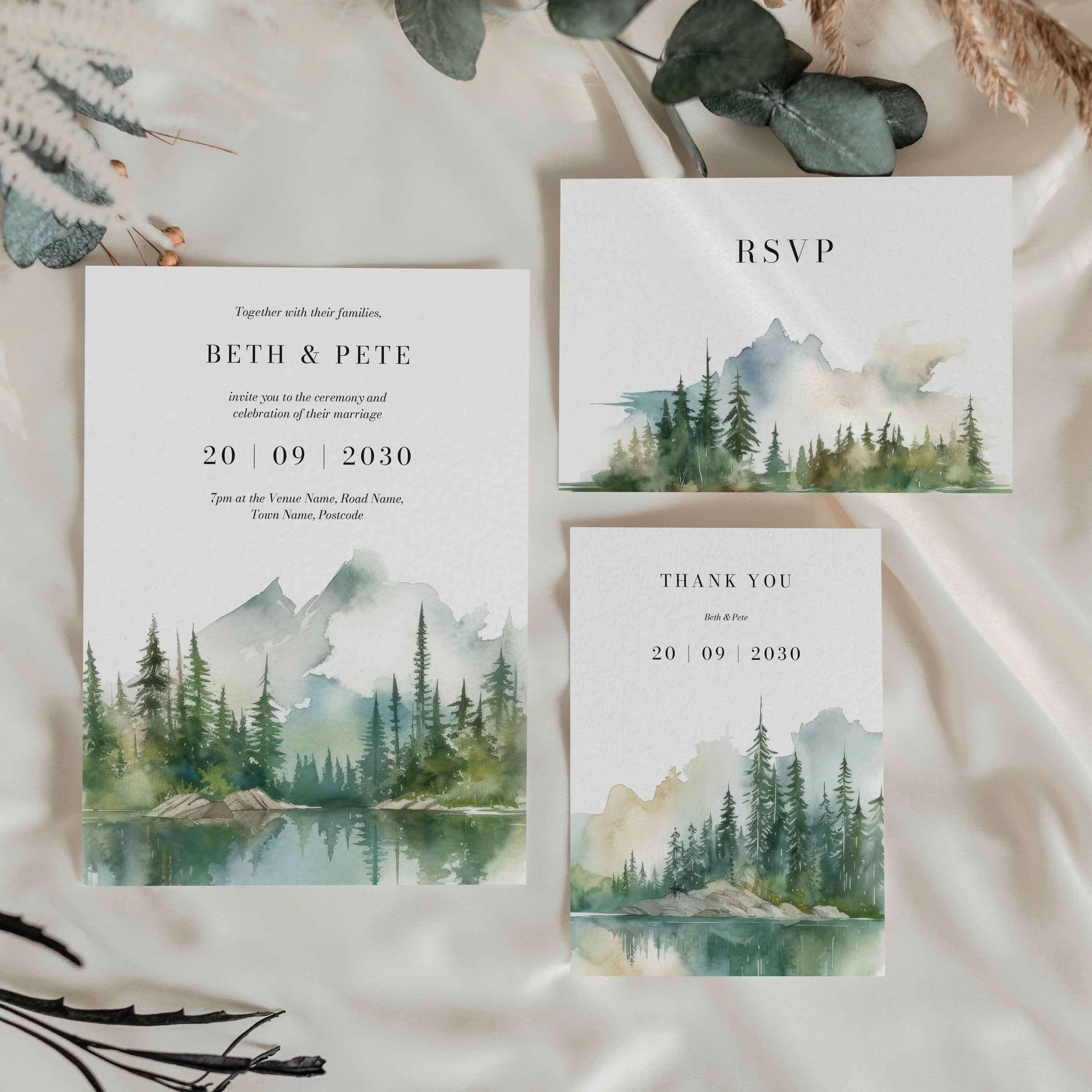 Wilderness wedding stationery suite flat lay showing invitations, RSVP cards and coordinating pieces with sage green mountain and pine forest watercolour design