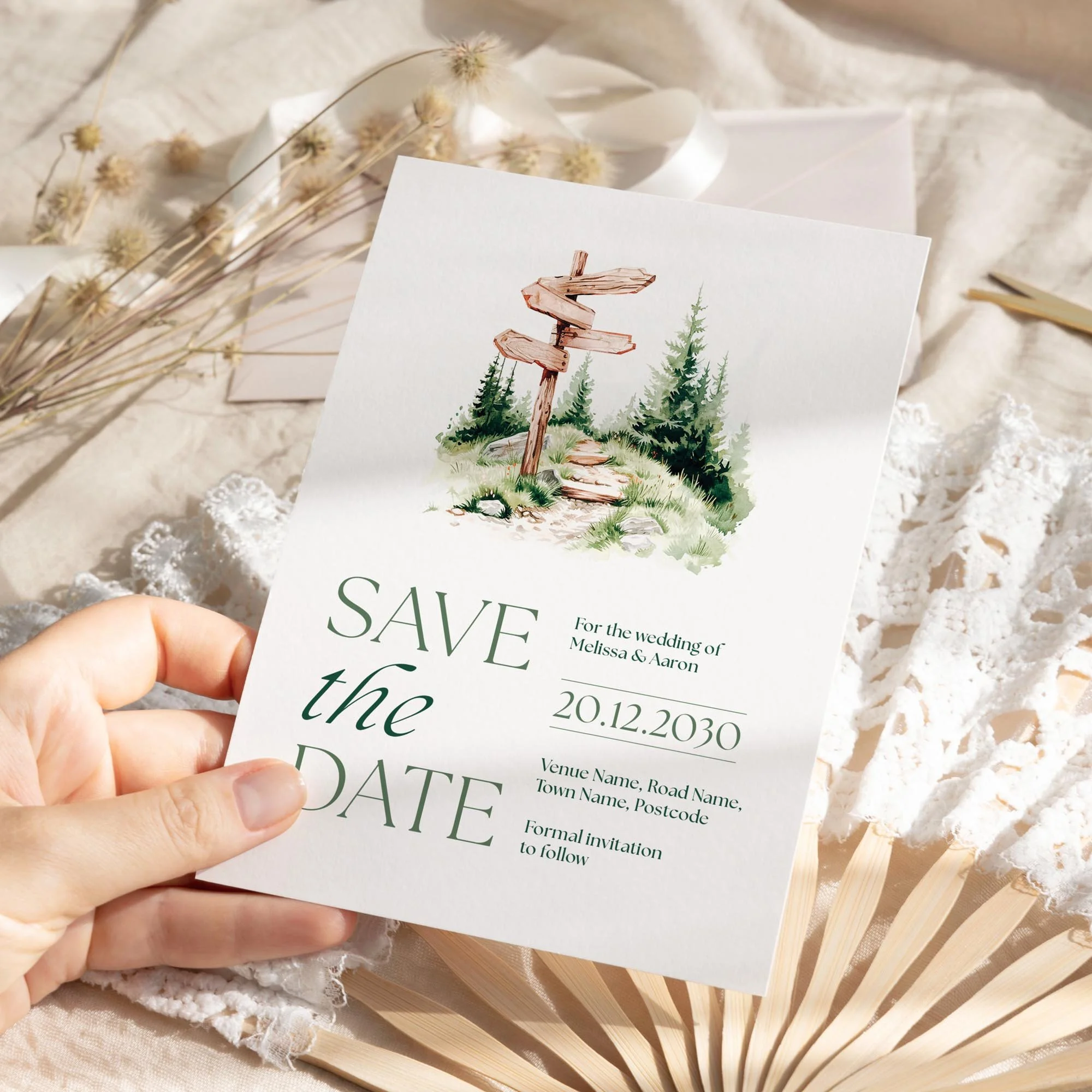 Person holding the Adventure Save the Date featuring a wooden signpost in a grassy field.