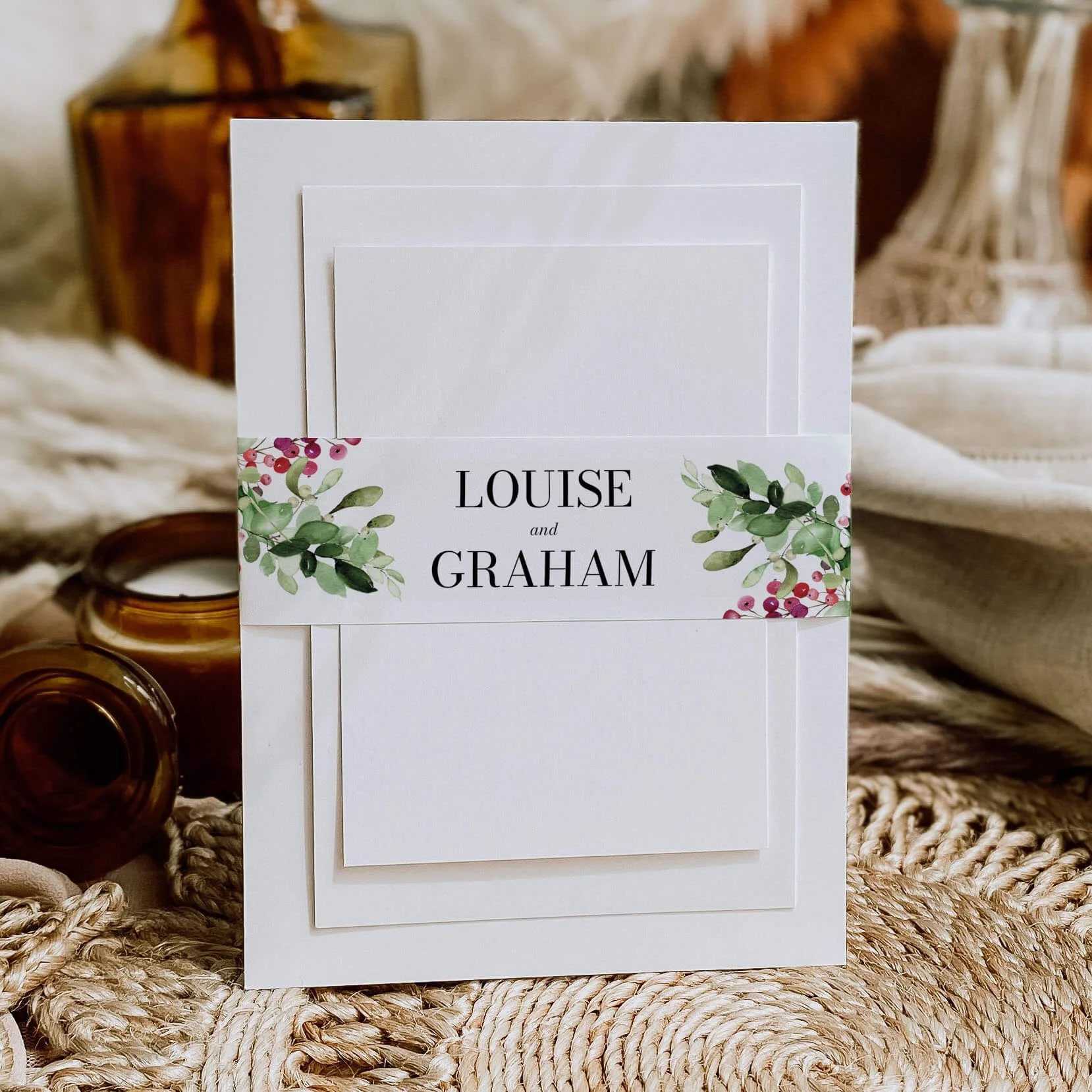 Festive personalised wedding belly bands with red winter berry and green foliage watercolour illustration wrapped around wedding invitations