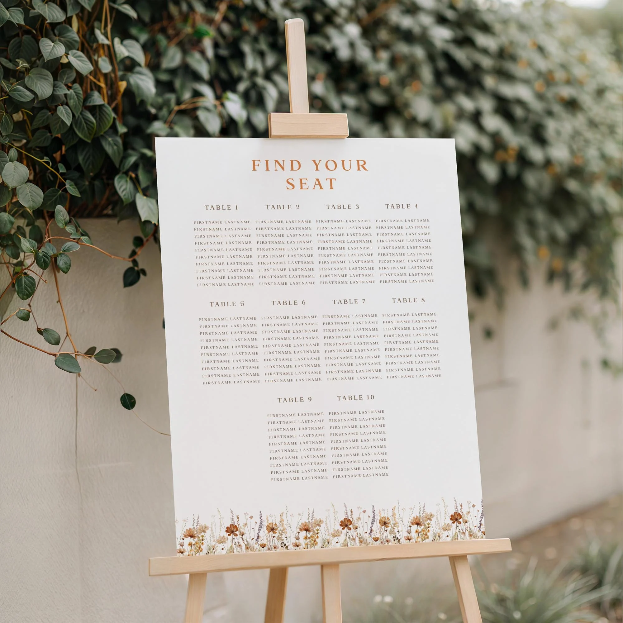 Field Harvest wedding seating plan displayed on a wooden easel, featuring an earthy autumn wildflower meadow design with multiple guest tables