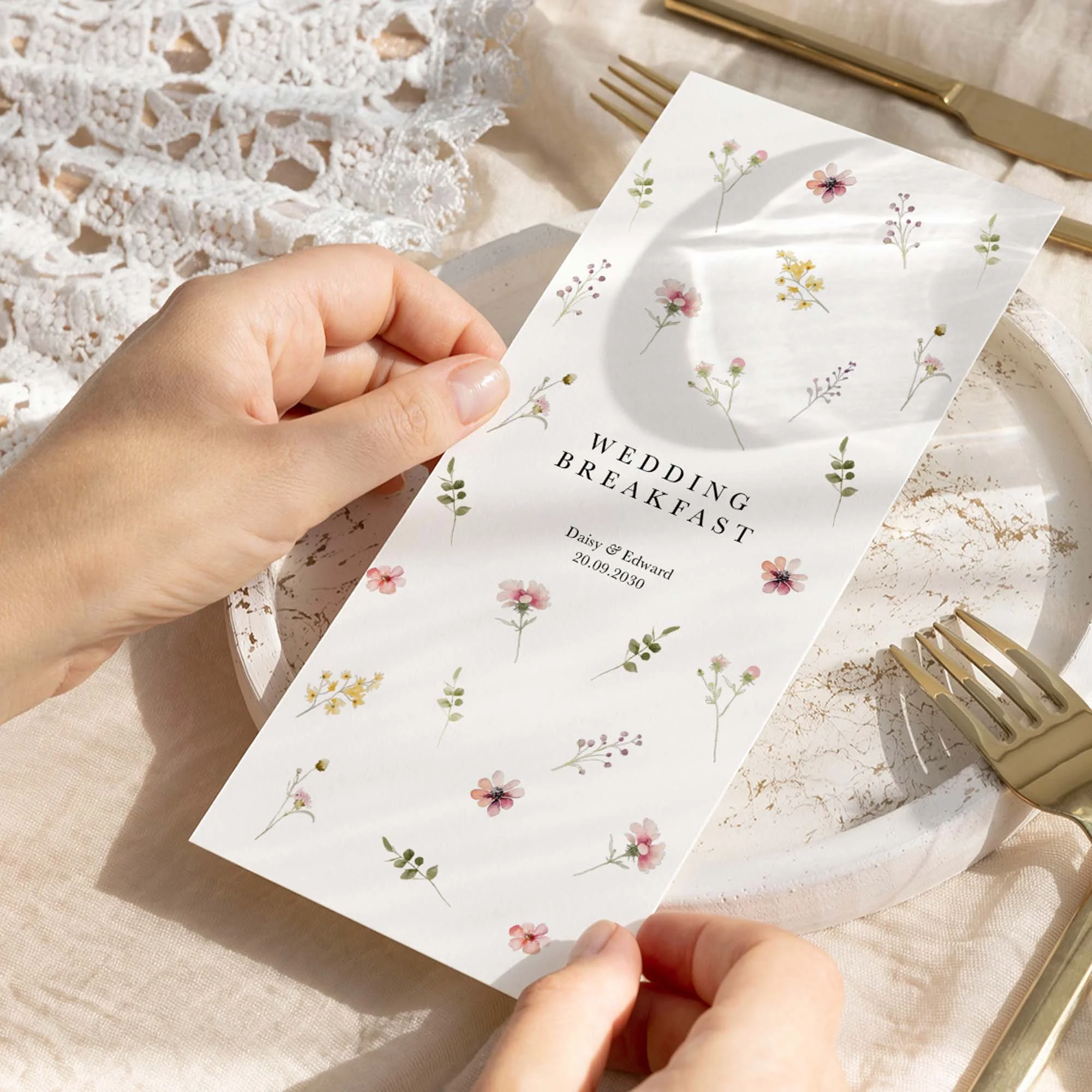 Hand holding a Flora wedding breakfast menu card with delicate scattered wildflower design in soft pastel tones