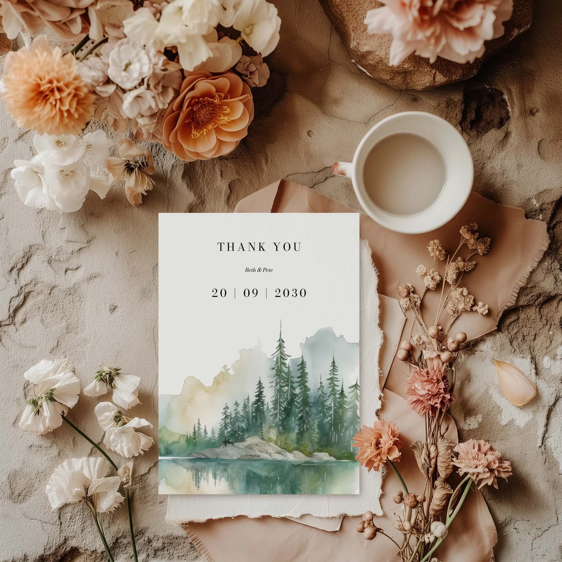 Wilderness wedding thank you card with watercolour mountain and pine forest design, styled with dried flowers and a white cup on a neutral background