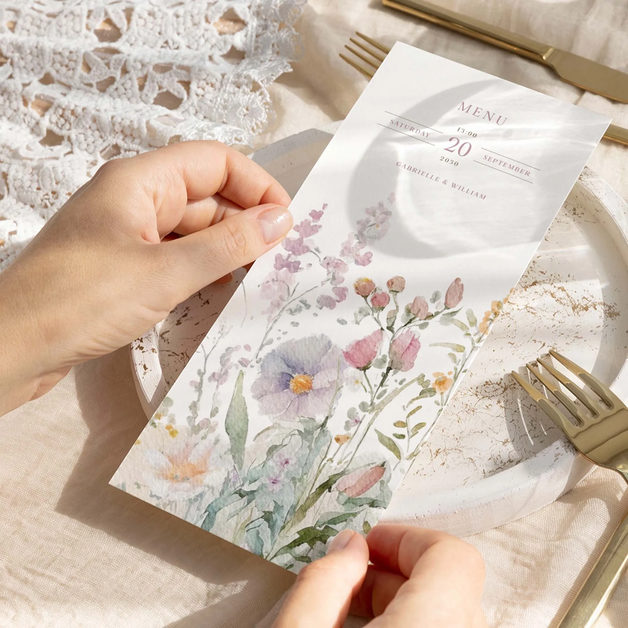 Hand holding a Field Powder wedding breakfast menu card with a dusty pink wildflower design in soft pastel tones