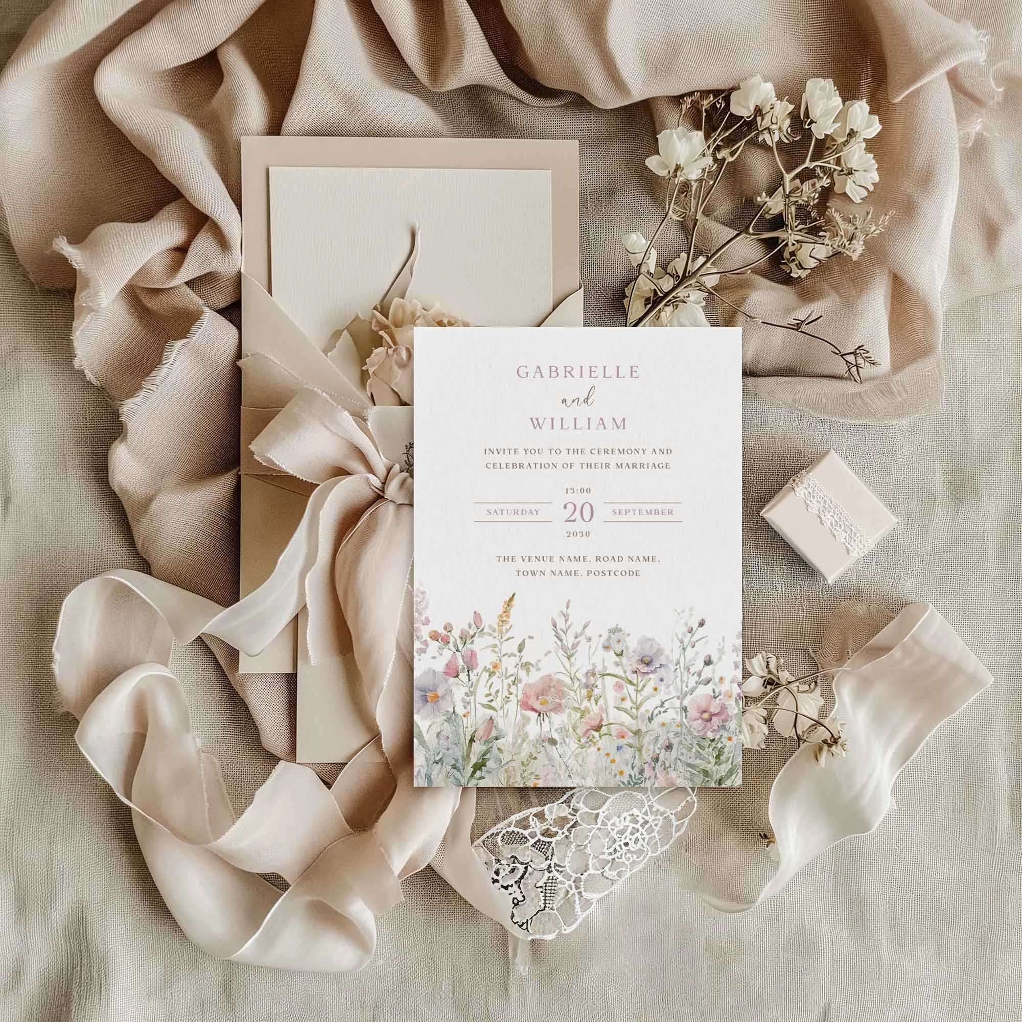 Field Powder wedding invitation featuring pastel wildflowers, displayed on linen fabric with dried flowers and a small gift box