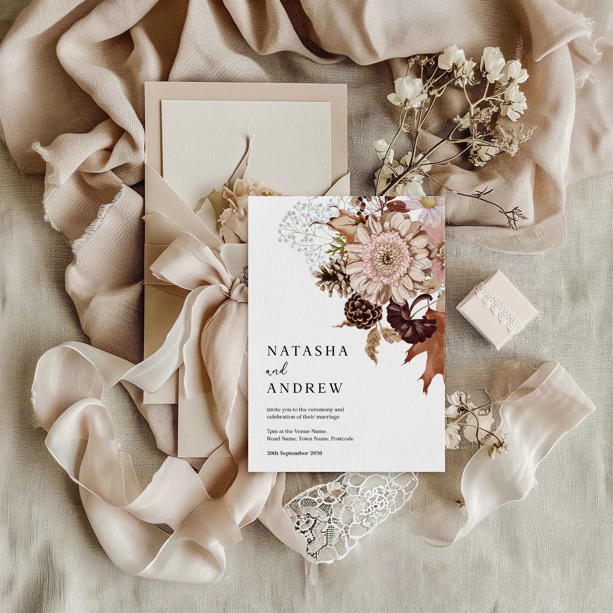Autumn floral wedding invitation flat lay featuring a rich botanical corner bouquet with dahlias, ferns and autumn leaves, displayed on cream linen with dried flowers and a small gift box