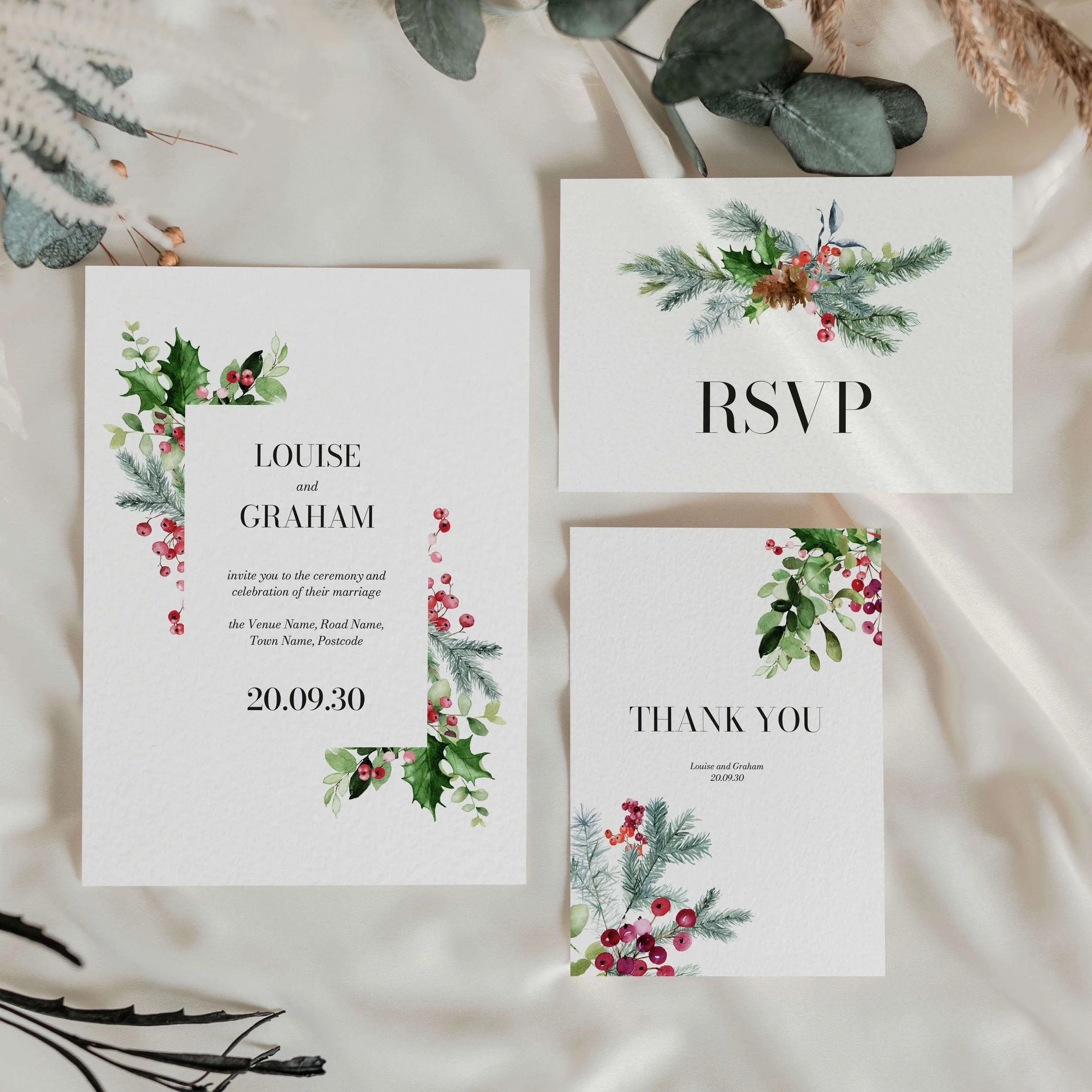 Festive wedding stationery suite flat lay showing invitations, RSVP cards and coordinating pieces with bold holly, red poinsettia and berry seasonal arrangement