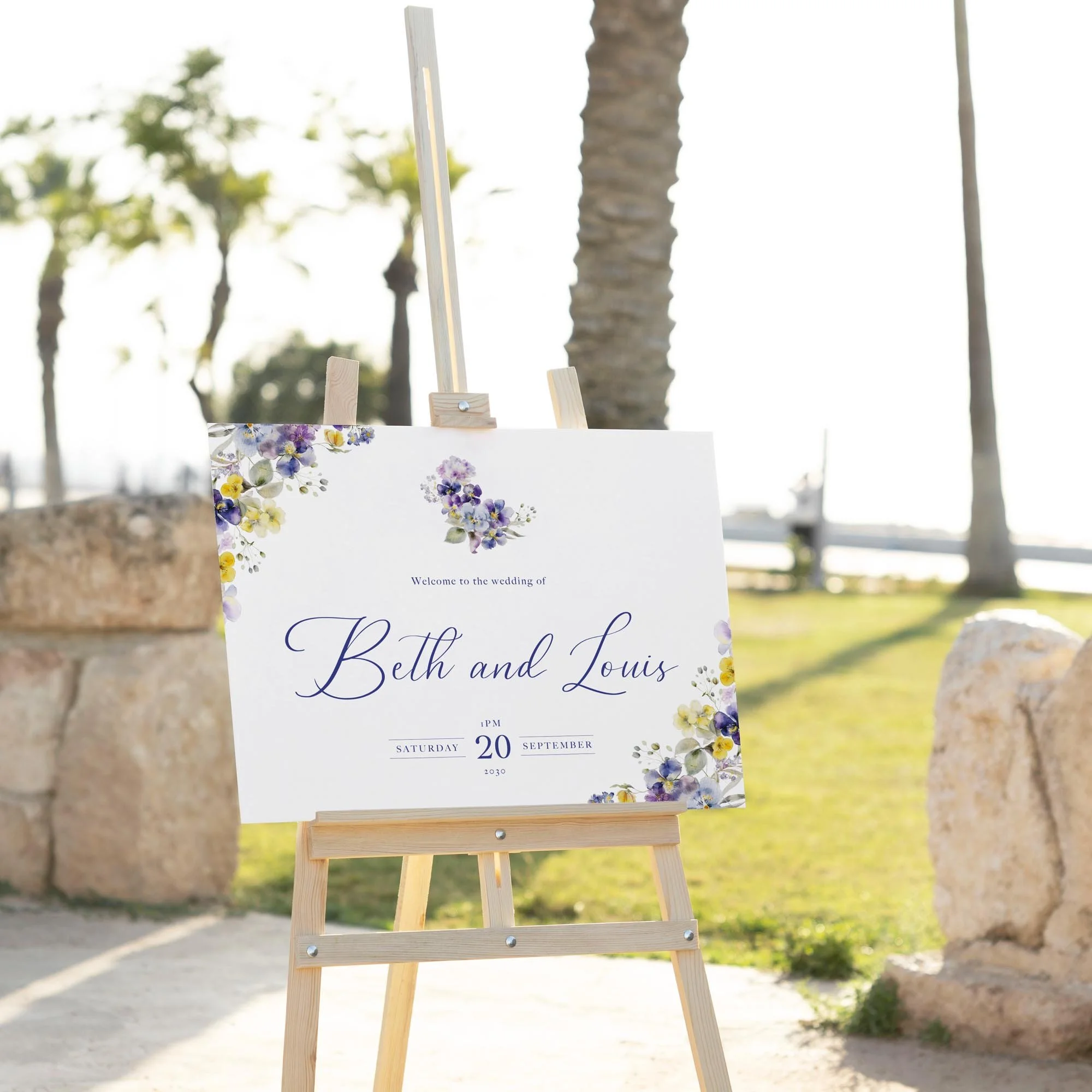 Violet and Yellow Floral wedding welcome sign displayed outdoors at a wedding venue on an easel