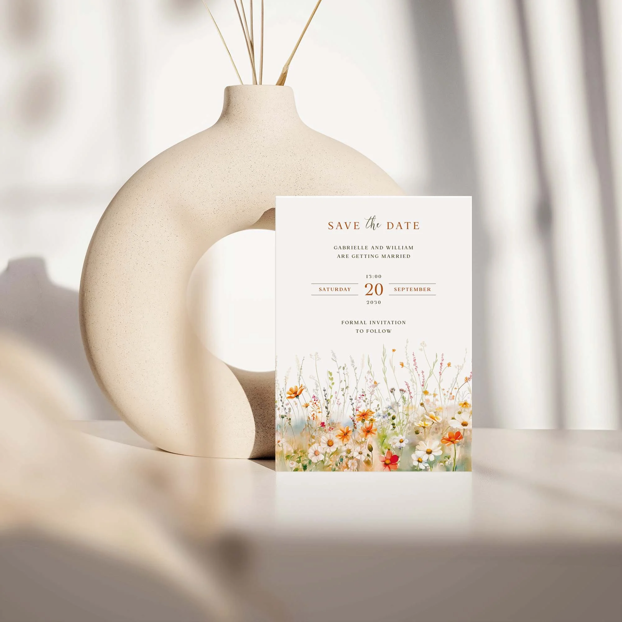 Field Vermilion save the date card with terracotta wildflower meadow design displayed against a cream ceramic vase on a neutral background