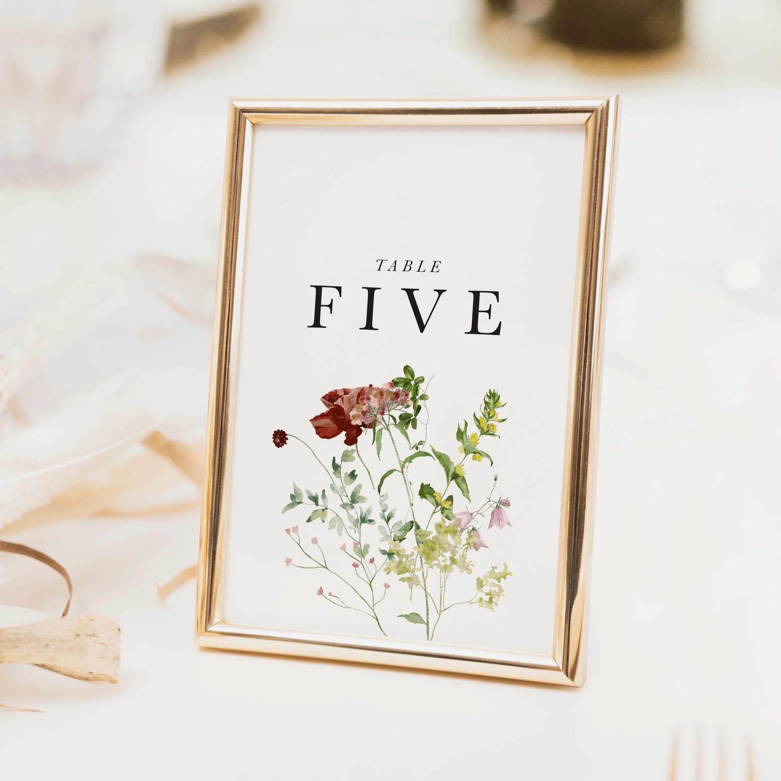 Meadow wedding table number with vibrant mixed wildflower and botanical illustration and spaced serif typography on luxury off-white card