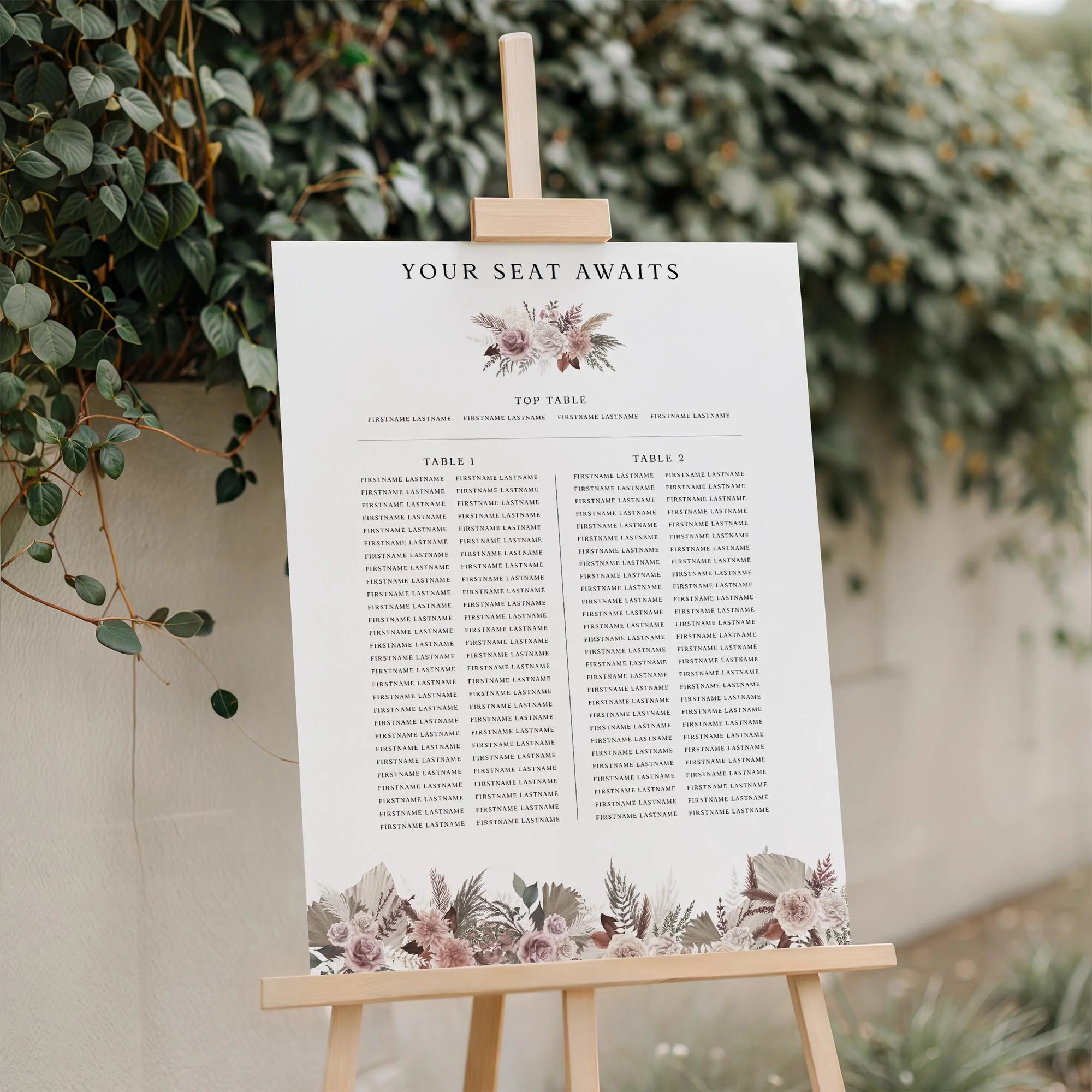 Blush Boho wedding seating plan displayed on a wooden easel, featuring pampas grass and blush pink floral design with multiple guest tables