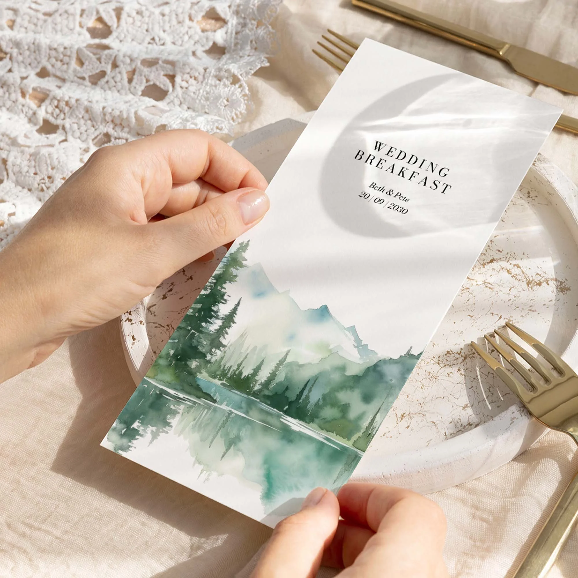 Hand holding a Wilderness wedding breakfast menu card with a serene watercolour mountain and pine forest lake landscape illustration