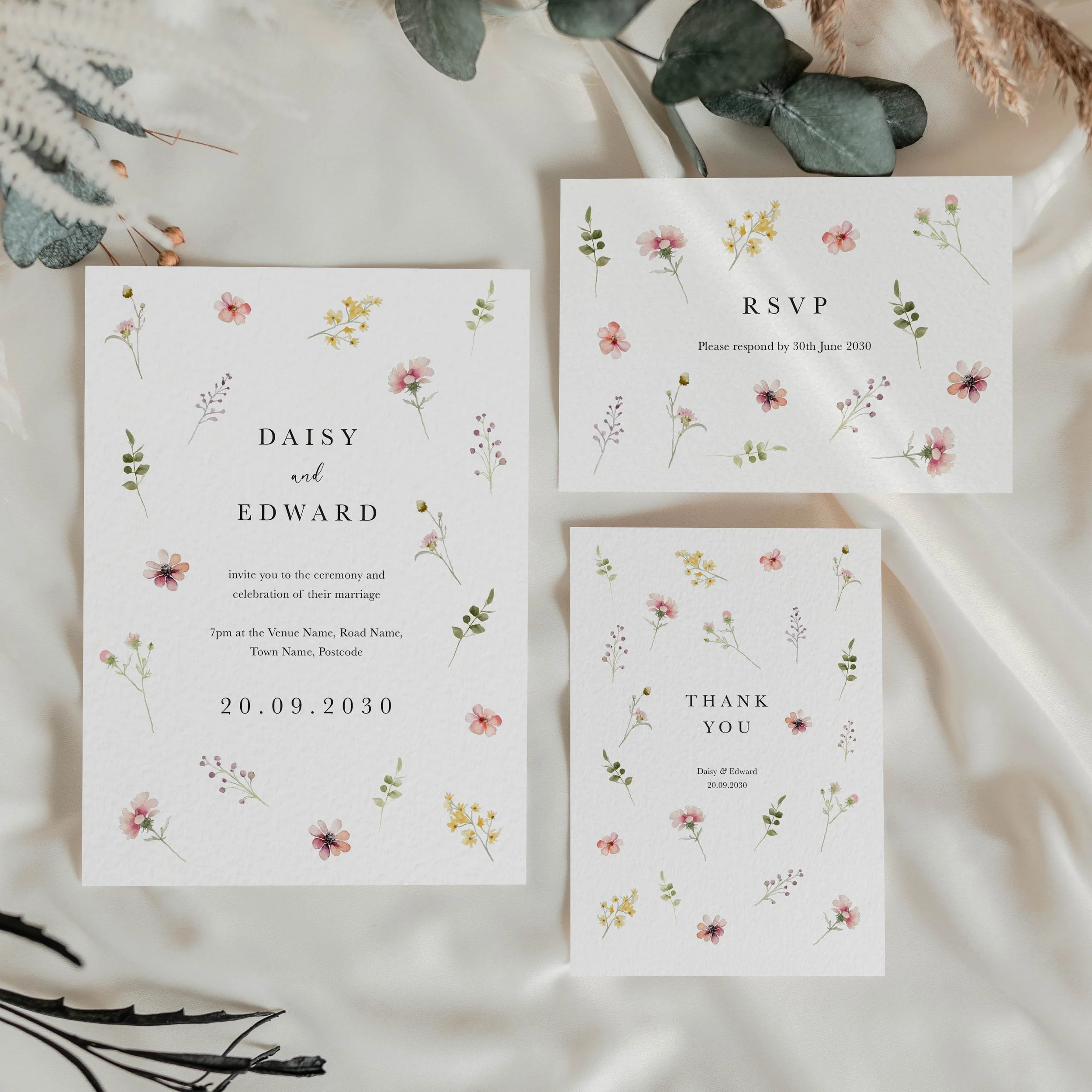 Flora wedding stationery suite flat lay showing invitations, RSVP cards and coordinating pieces with scattered pastel wildflower design