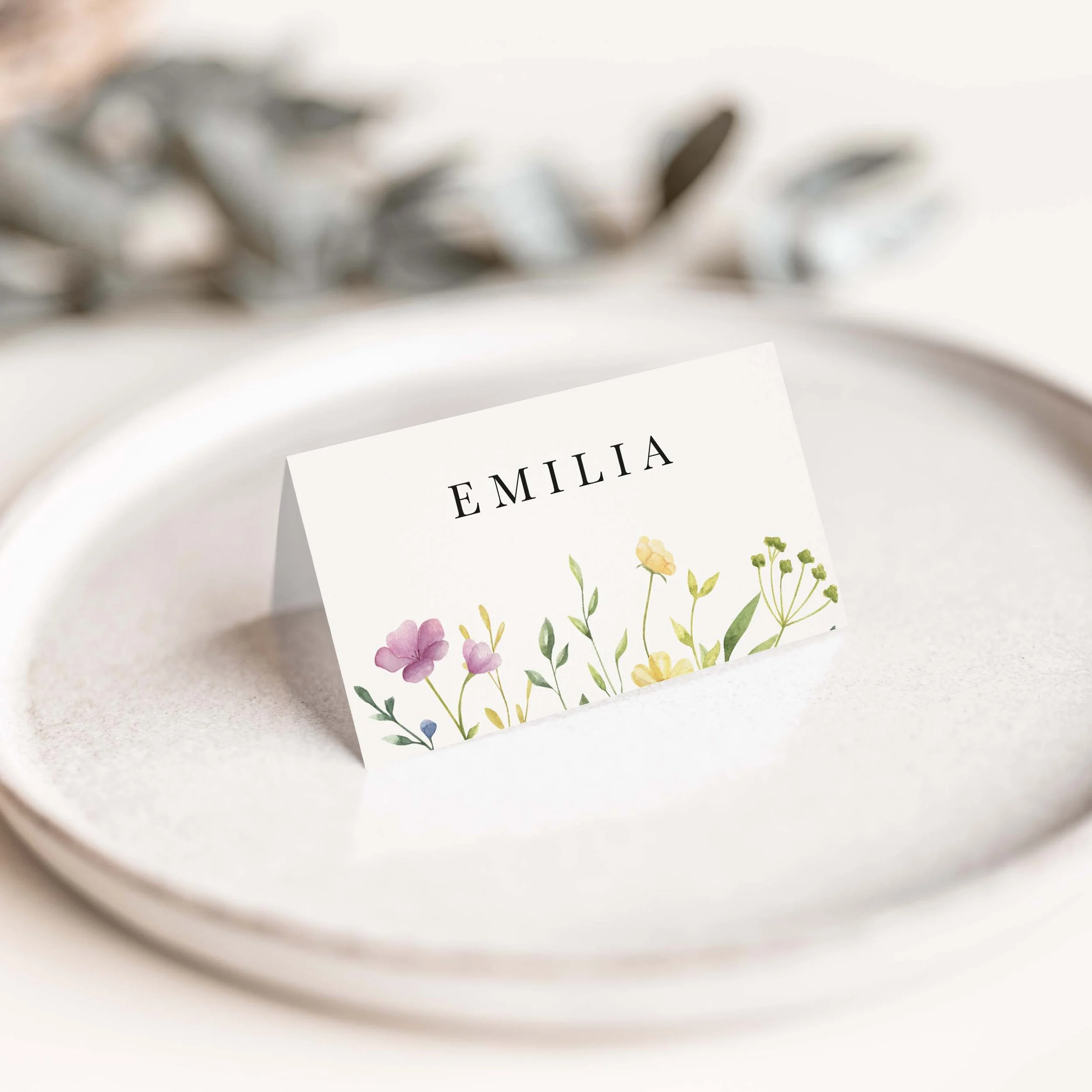 Wildflower wedding place card with vibrant colourful scattered wildflower botanical illustration and clean serif guest name typography on luxury off-white card