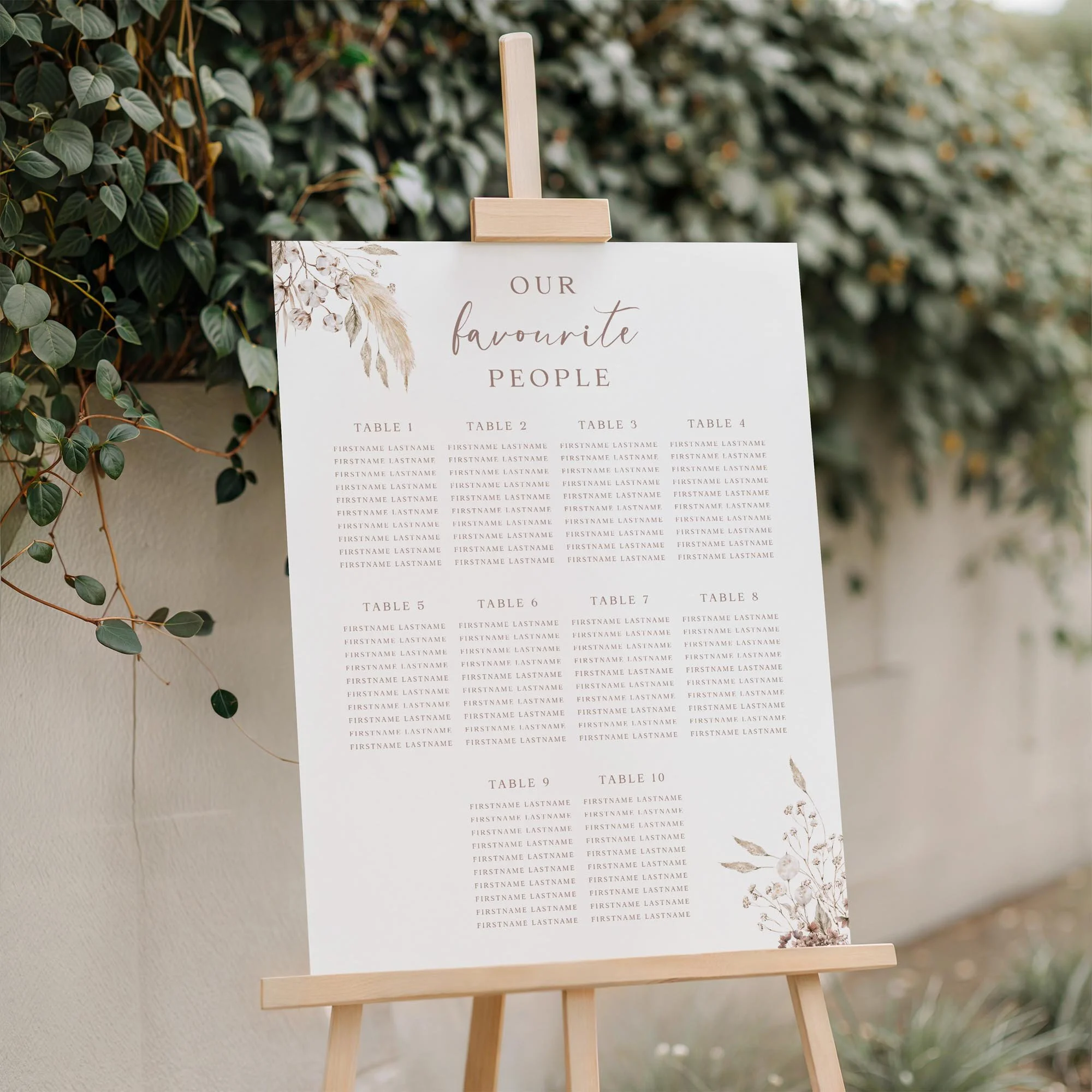 Boho wedding seating plan displayed on a wooden easel, featuring a neutral dried flower botanical design with multiple guest tables