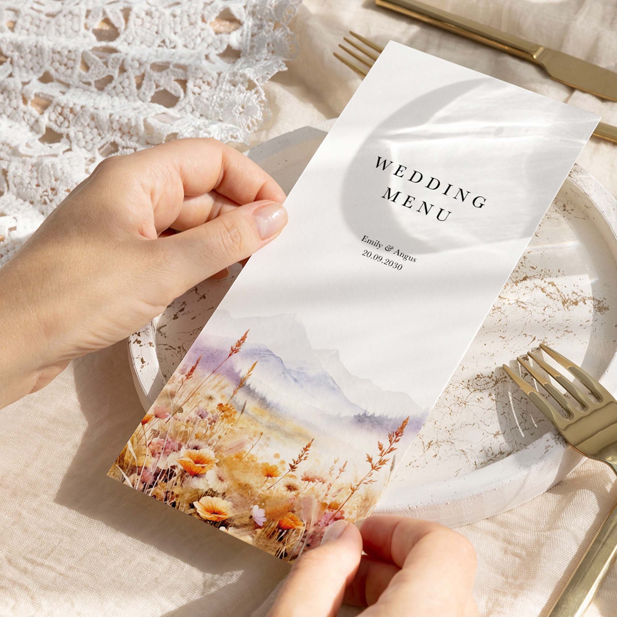 Hand holding a Scenic wedding breakfast menu card with a watercolour countryside landscape in soft purple and golden amber tones