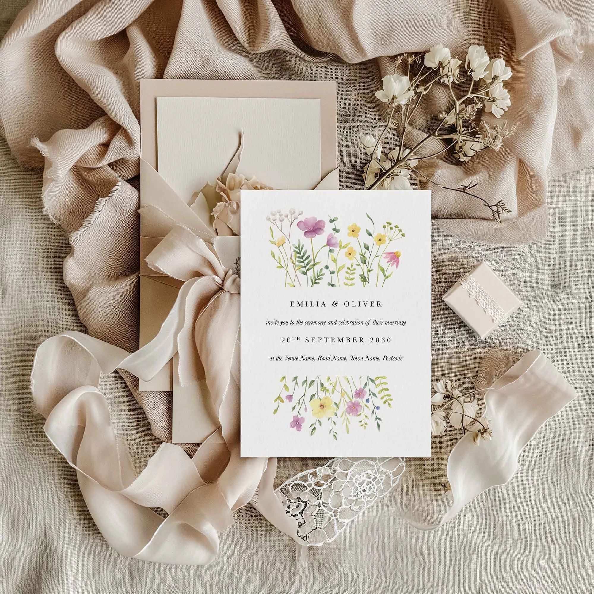 Wildflower wedding invitation flat lay featuring rustic wildflowers, displayed on sage linen fabric with dried flowers and a small gift box