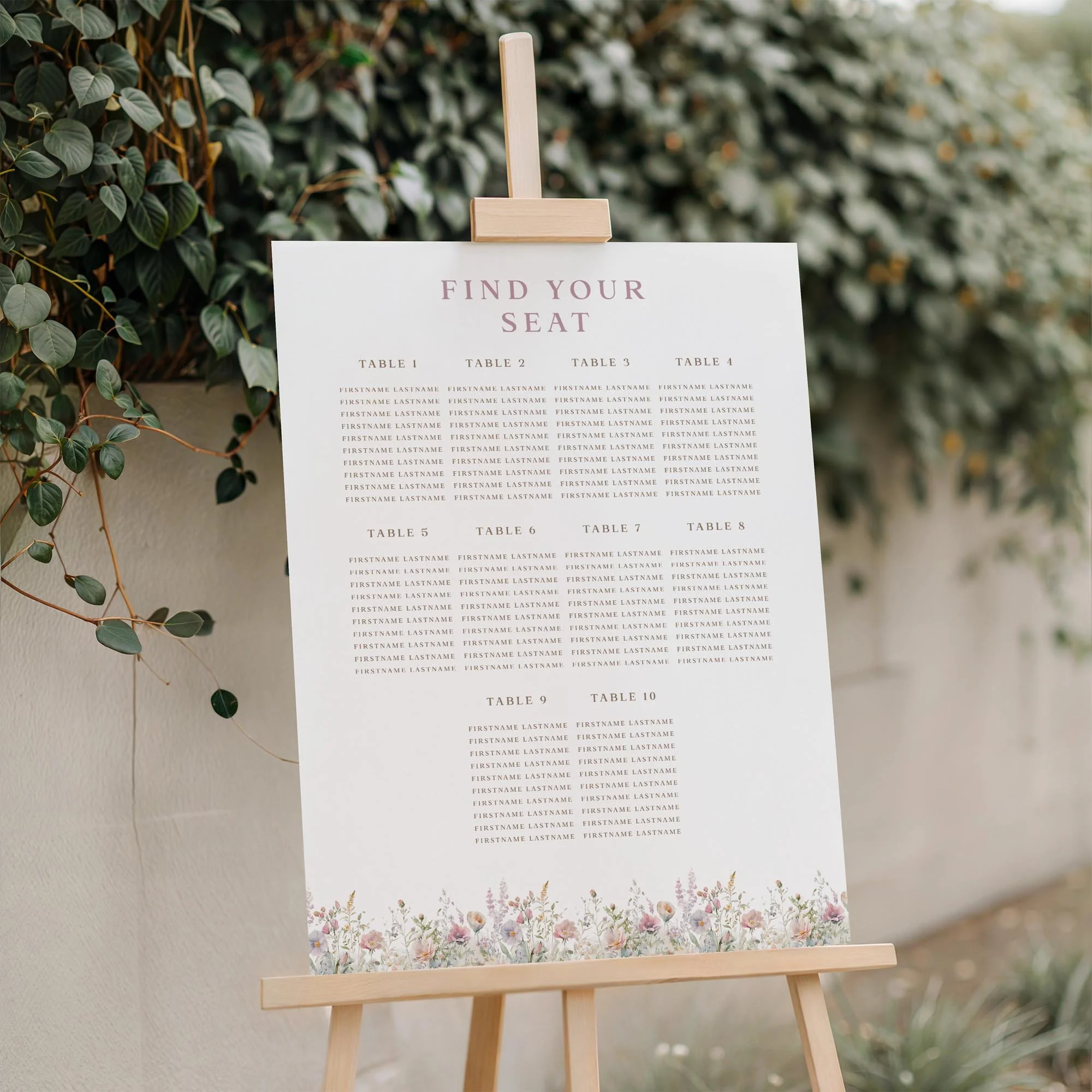 Field Powder wedding seating plan displayed on a wooden easel, featuring a dusty pink pastel wildflowers with multiple guest tables