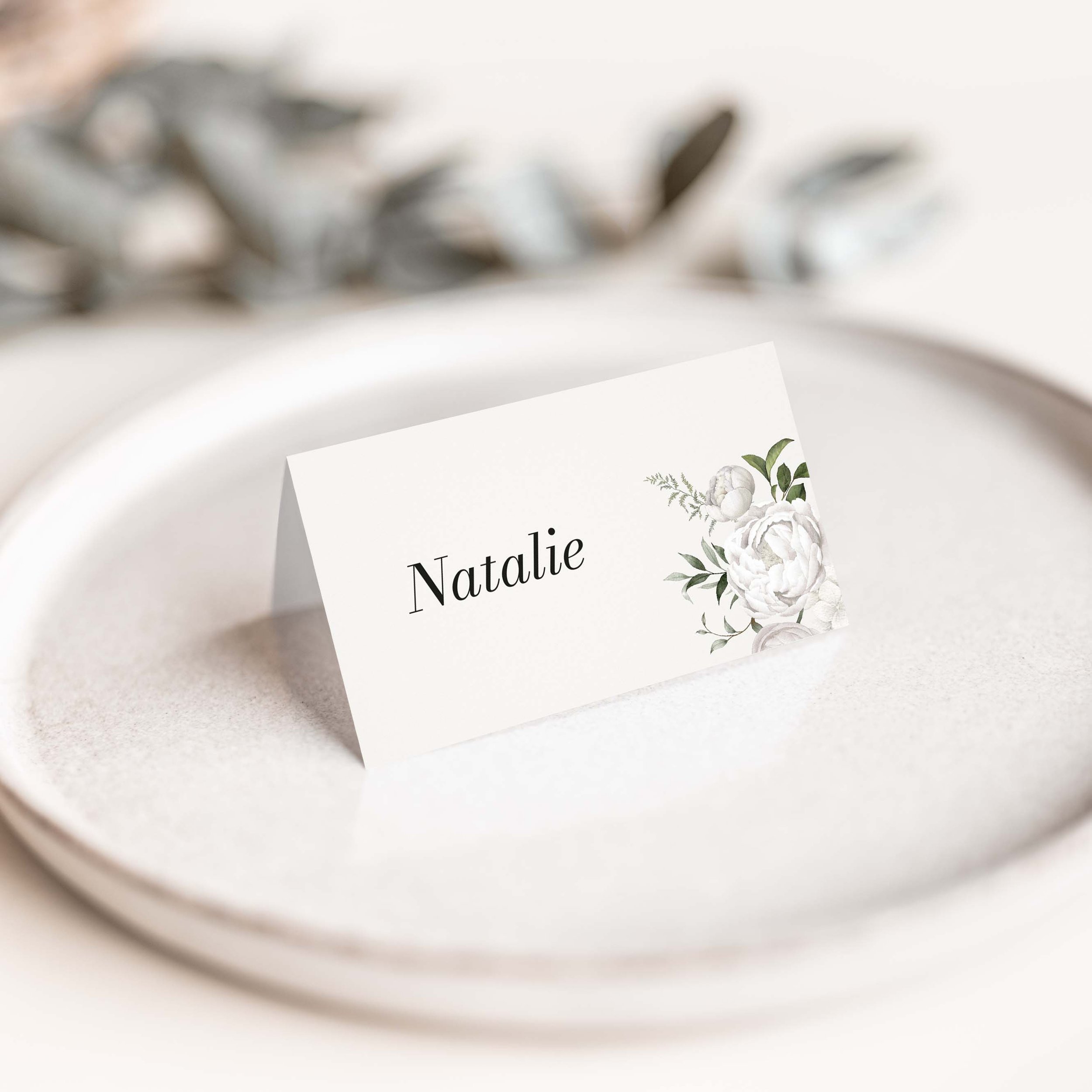 White Floral wedding place card with delicate white and green botanical floral illustration and flowing script guest name on luxury off-white card