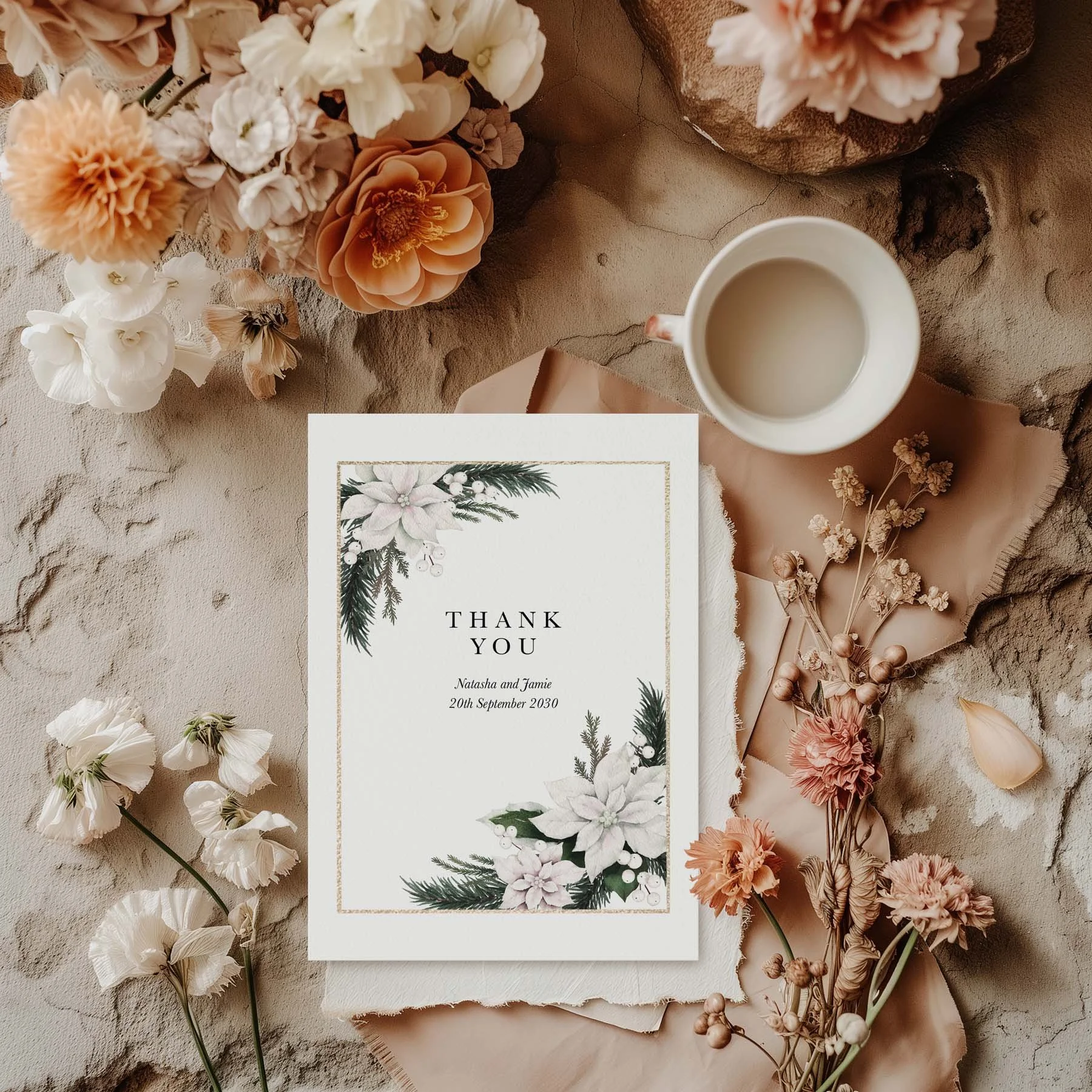 Winter Frost wedding thank you card with a gold frame and white poinsettia corner arrangement, styled with dried flowers and a white cup on a neutral background