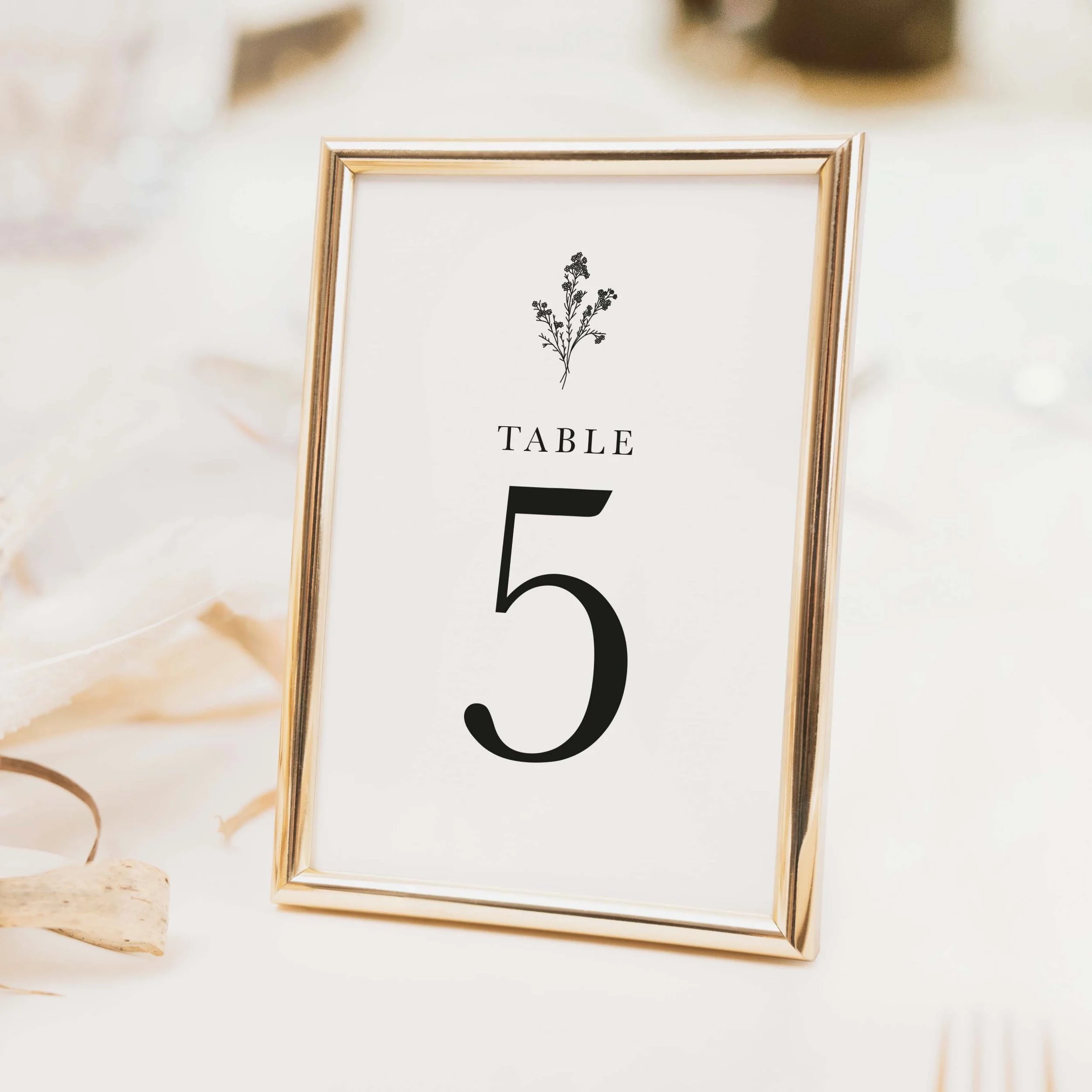 Monogram wedding table number with small decorative monogram motif above large bold numeral typography on luxury off-white card