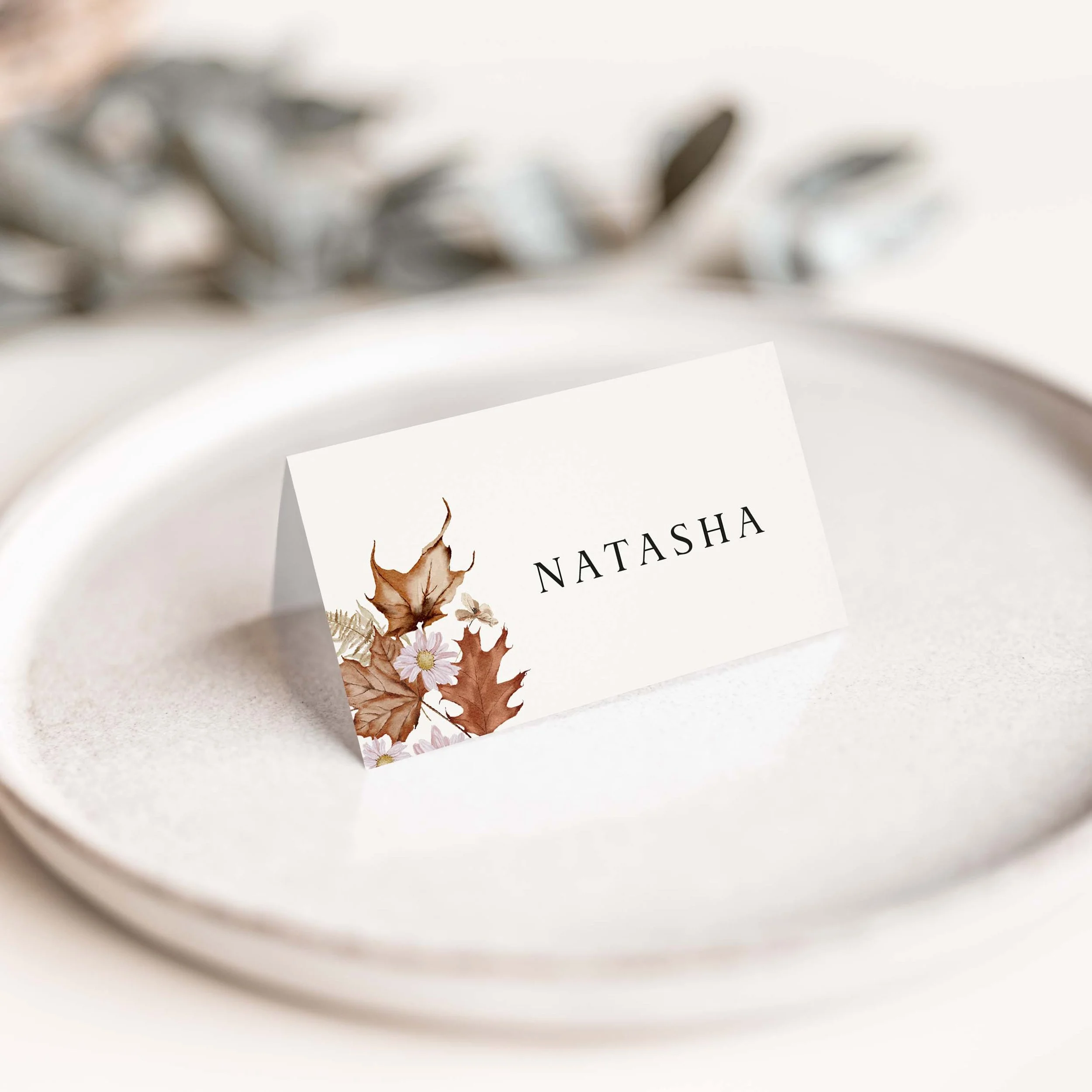 Autumn wedding place card with seasonal autumn leaf illustration and elegant serif typography on luxury off-white card