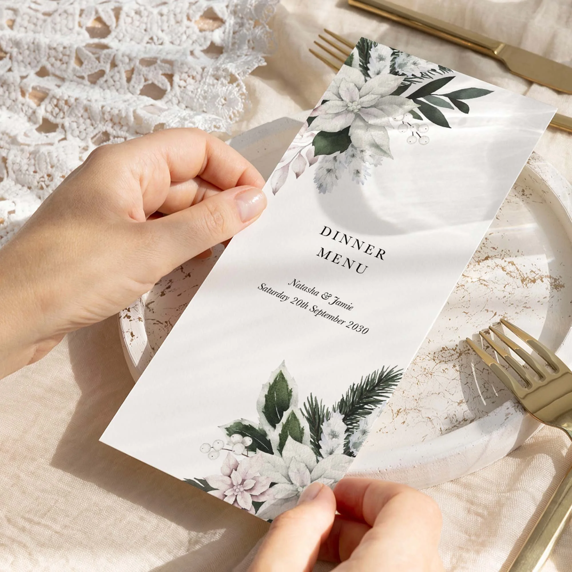 Hand holding a Winter Frost wedding breakfast menu card with a white poinsettia and pine botanical illustration