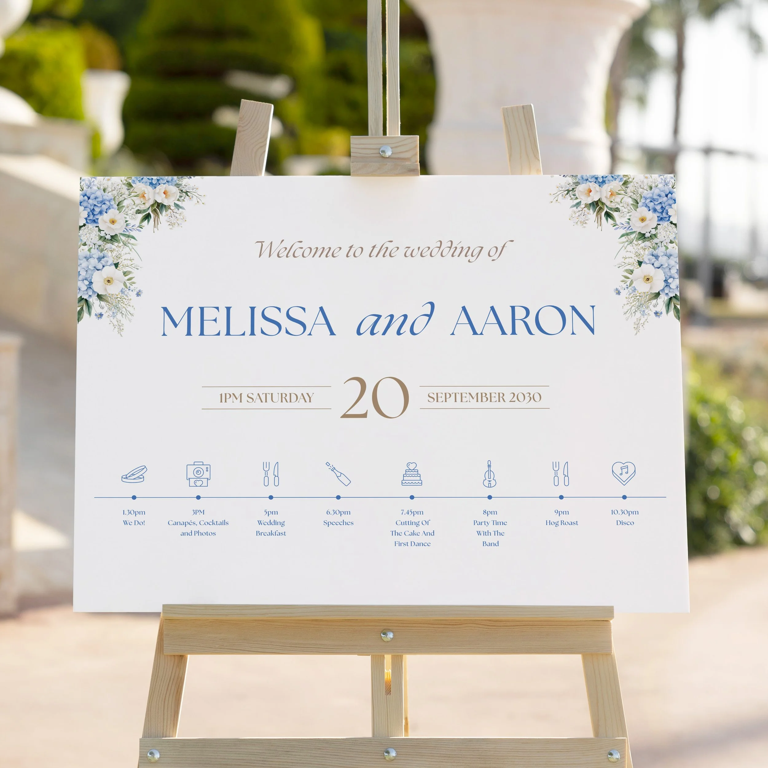 Close-up of Serenity Wedding Welcome Sign on easel with top corner blue floral details and timeline.