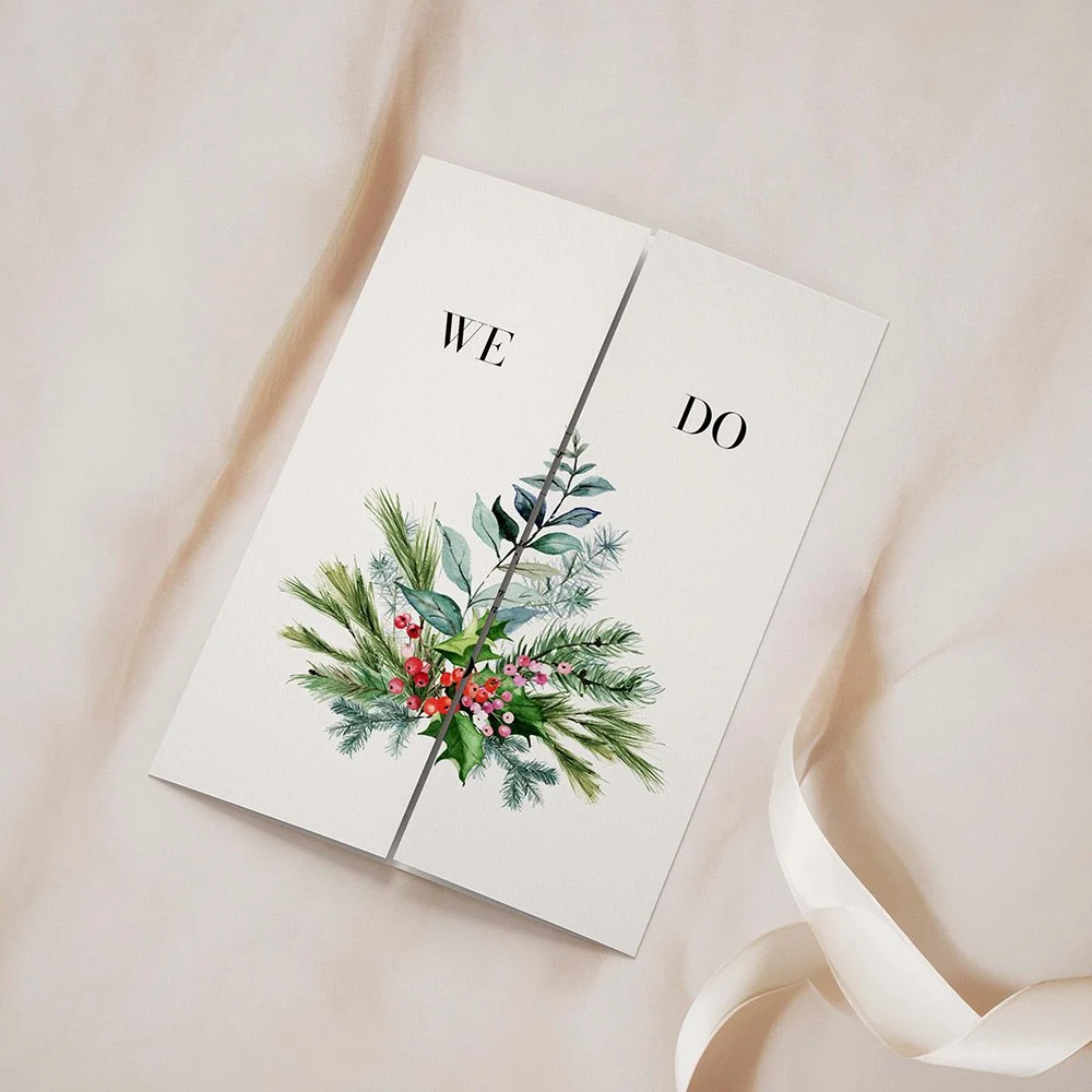 Festive Collection Frame gatefold invitation closed, showcasing pine leaves, pinecones, and winter foliage framing the wedding details.