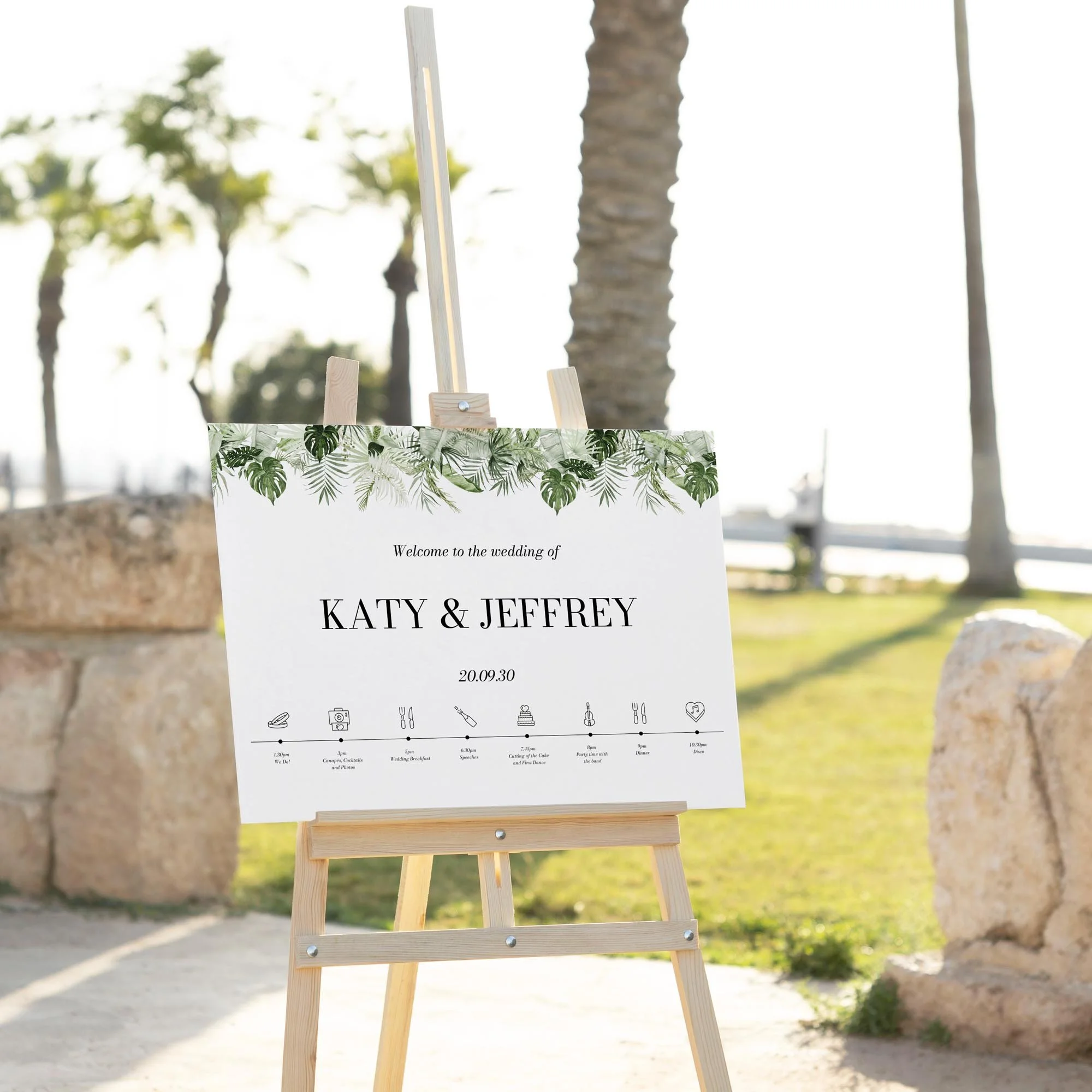 Tropical Leaves with an Order of the Day wedding welcome sign displayed outdoors at a wedding venue on an easel