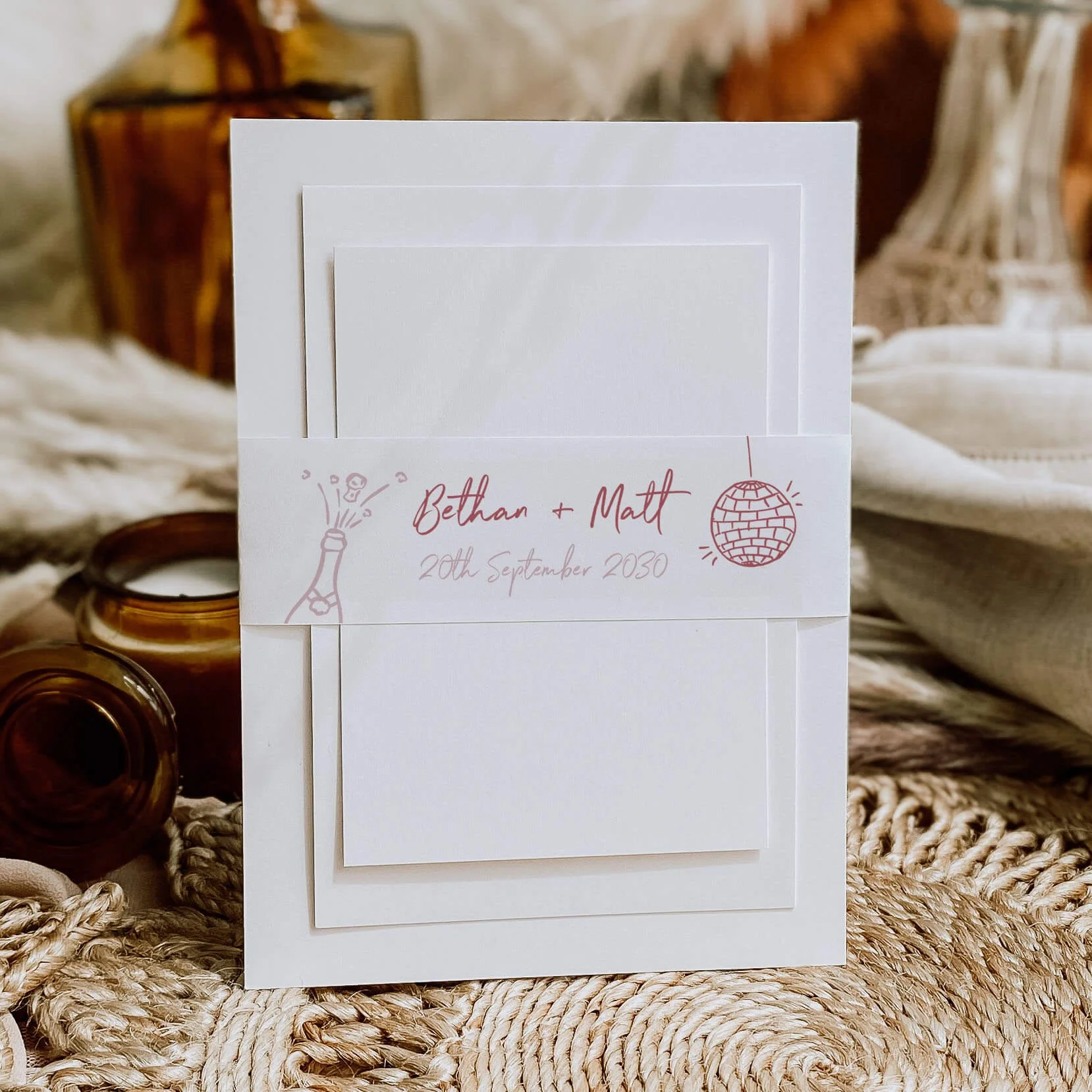 Whimsical Pink personalised wedding belly bands with pink champagne bottle and disco ball line-art illustration and script names wrapped around wedding invitations